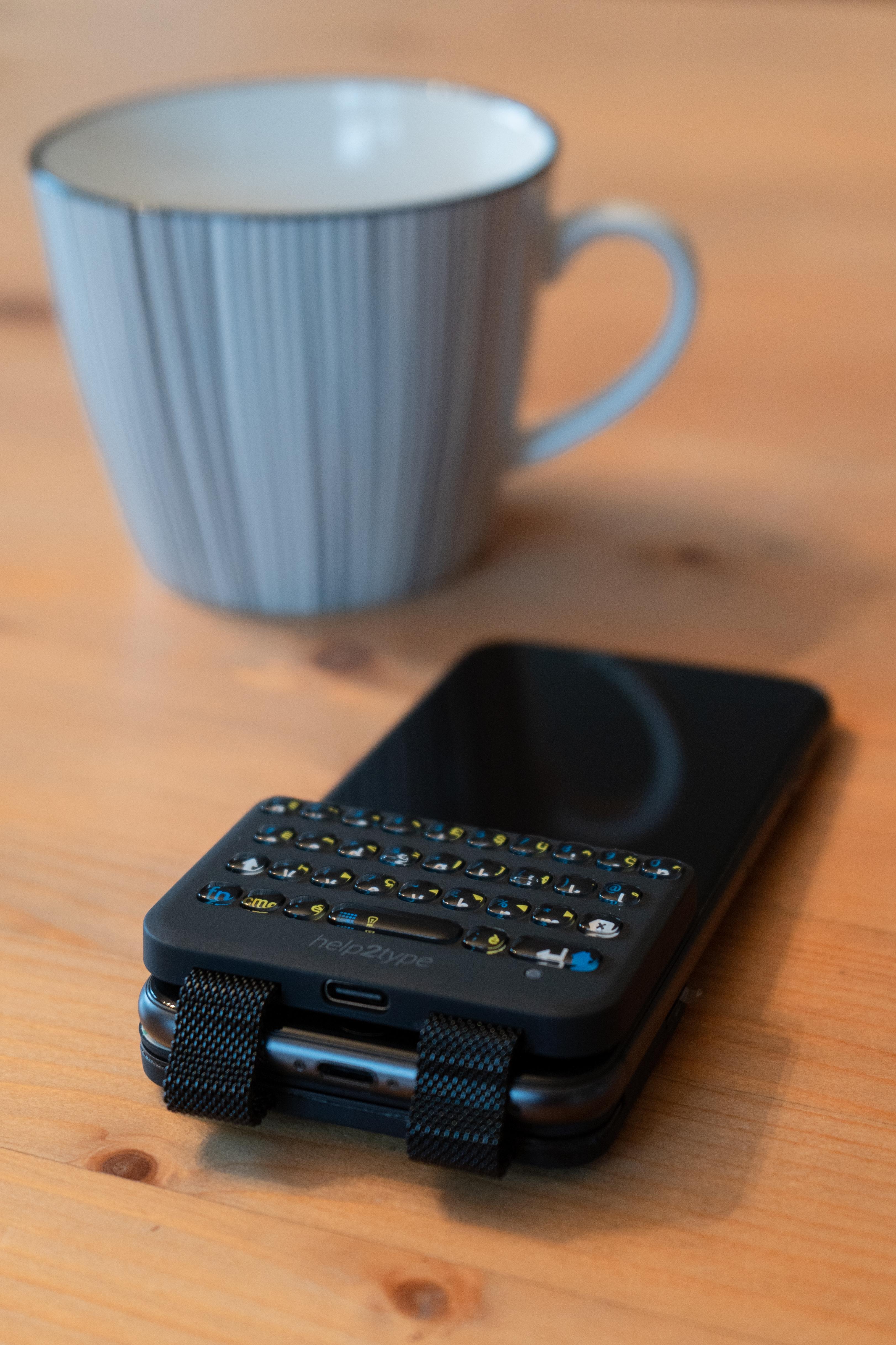 help2type keyboard on a smartphone placed on a table next to the phone is a blue mug