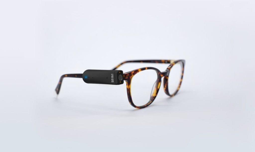Image shows a pair of tortoiseshell glasses with an OrCam MyEye Pro attached to the arm of the glasses