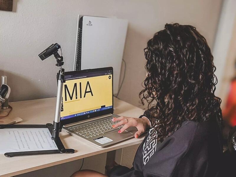 A lady using the OrCam MyEye 3 Pro in it's stand it's been connected to her laptop and she is using the device as a magnifier, on the laptop screen you can see the enlarged text