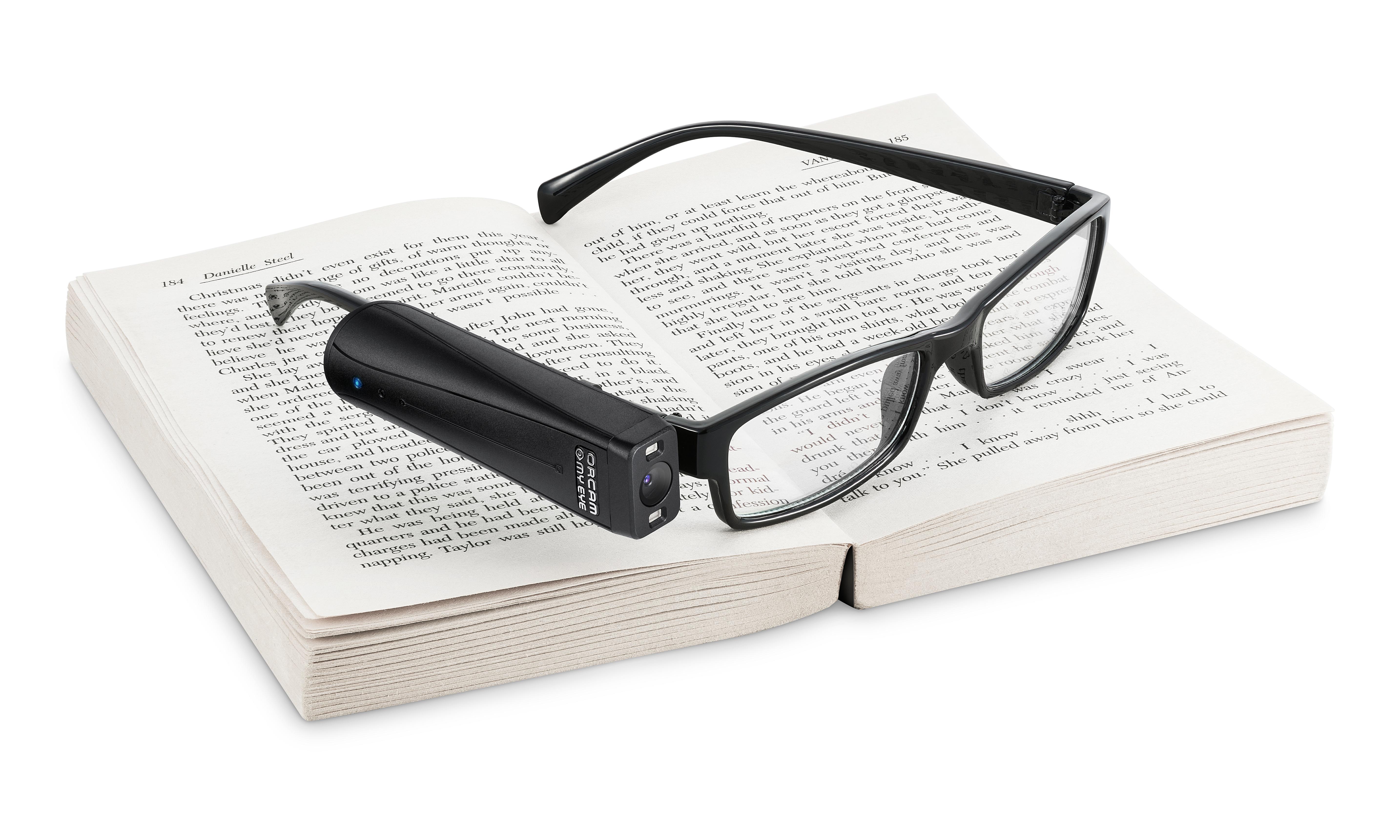 OrCam MyReader 2.0 attached to a pair of glasses resting on an open book