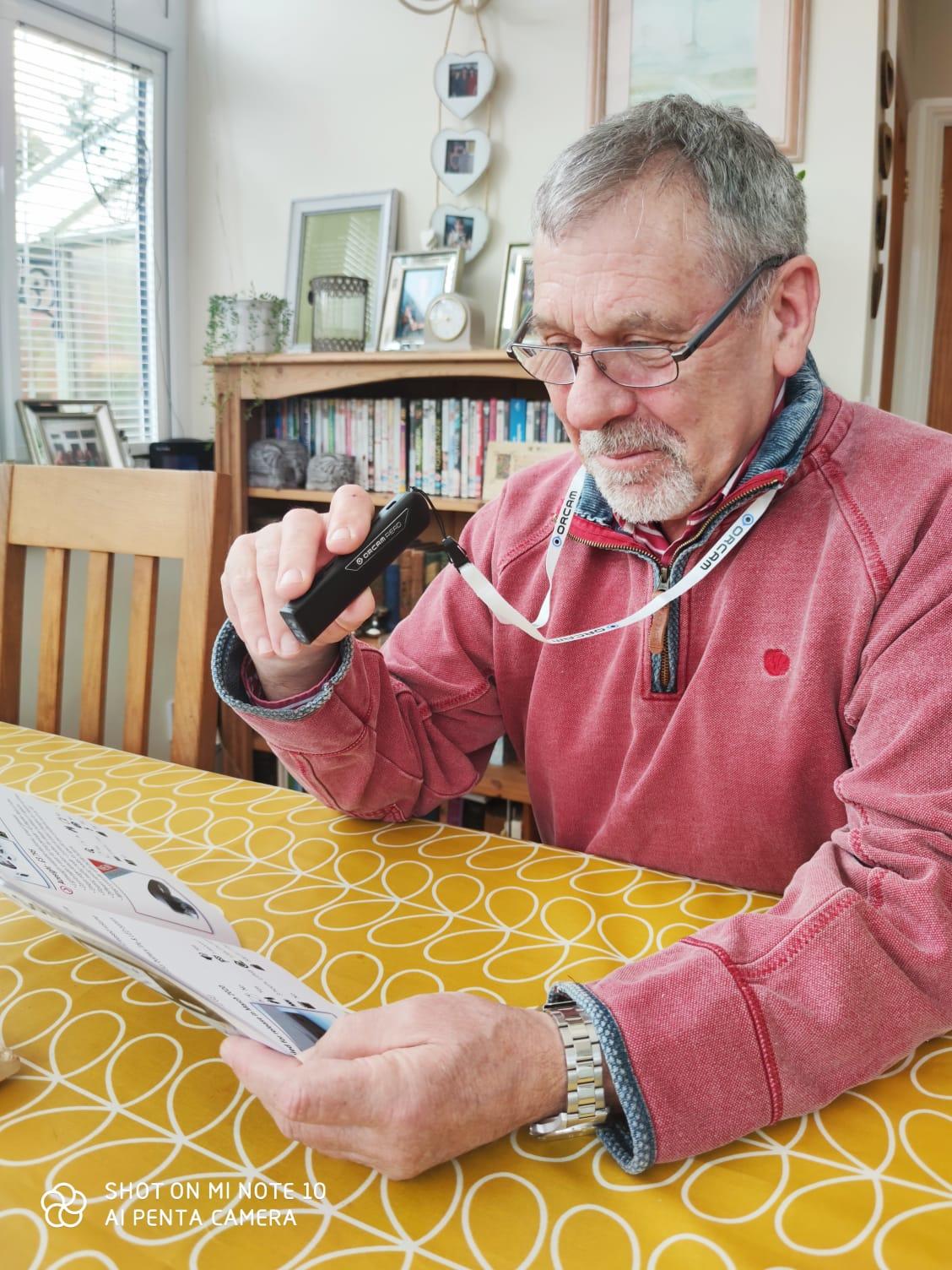 an older gentleman using his orcam read smart on a lanyard to read a magazine