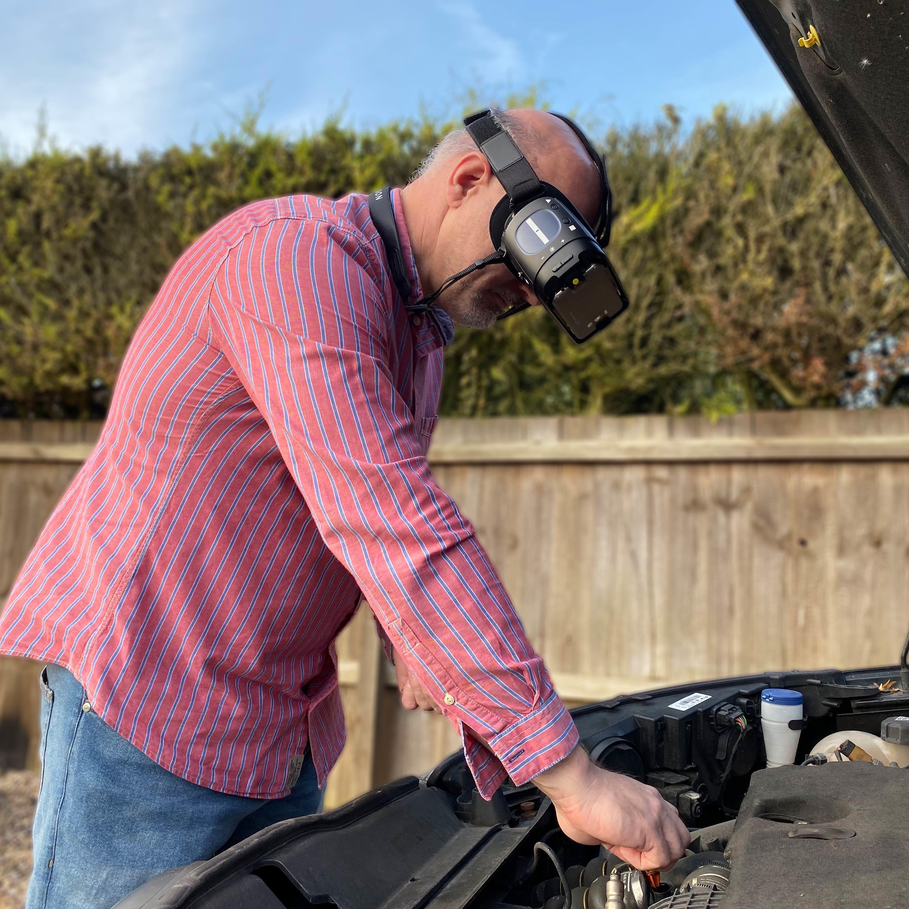 A man using his IrisVision wearable magnifier to repair his car engine