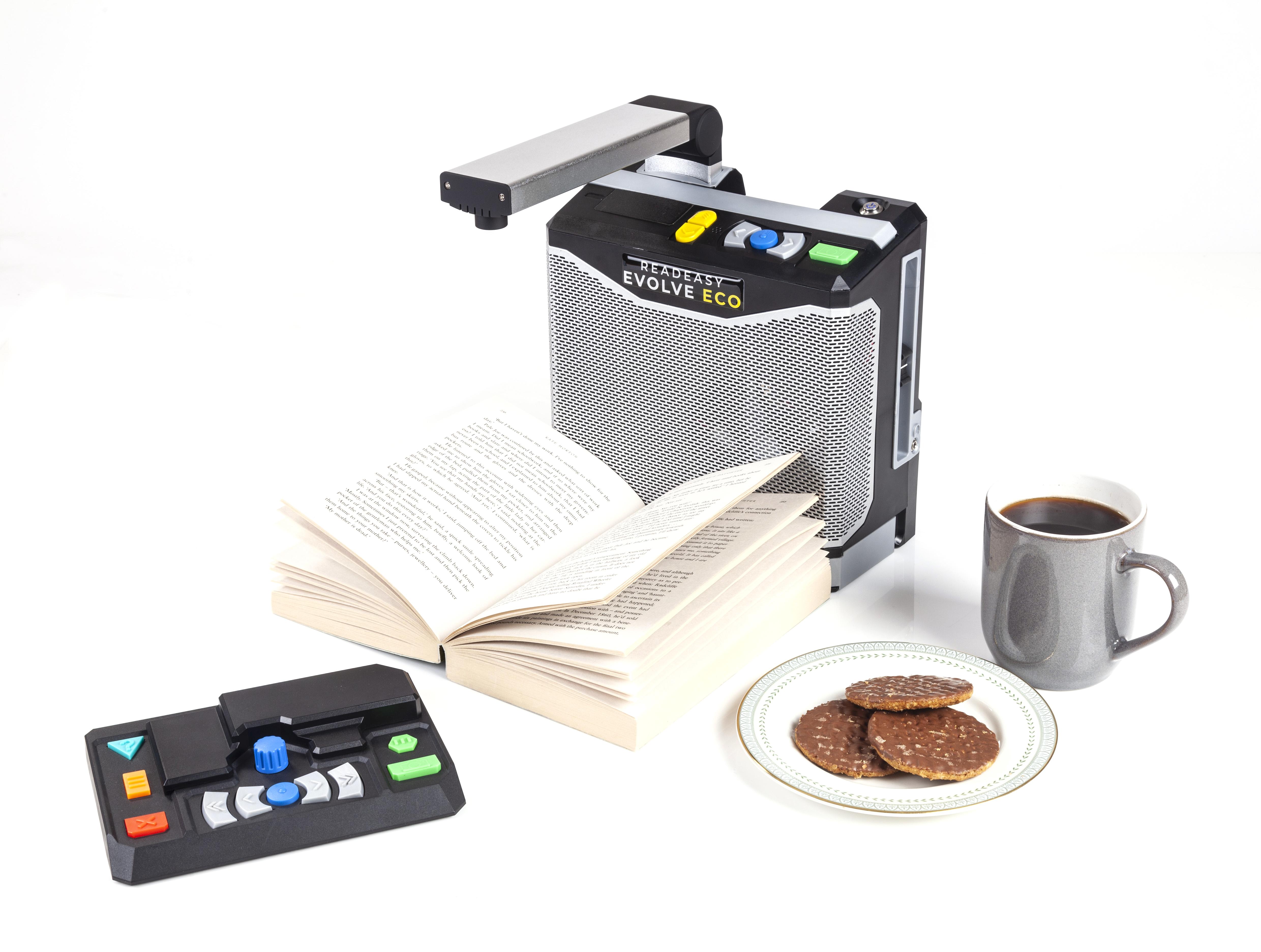 ReadEasy Evolve ECO capturing a book in front of the book is the optional feature pack. To the right of the ReadEasy evolve eco is a grey mug of black coffee a plate with 3 chocolate covered digestive biscuits