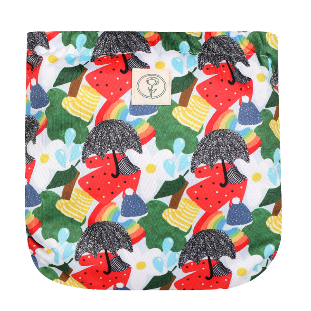 Image shows back of a reusable nappy wrap with small Bombacio logo label and pattern of umbrellas, wellies, splashes, jumpers, wooly hats and flowers in reds, blues, yellows, whites.