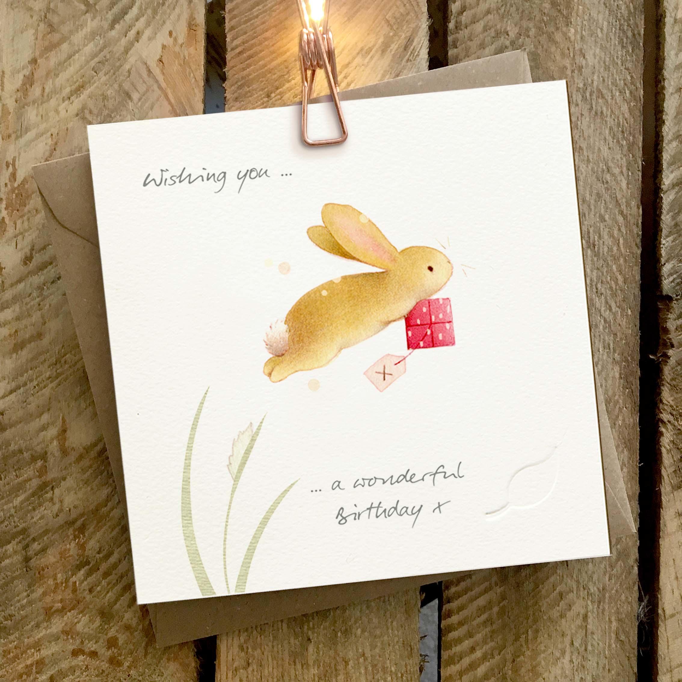Card featuring a cute rabbit carrying a little present, and leaping into the air.