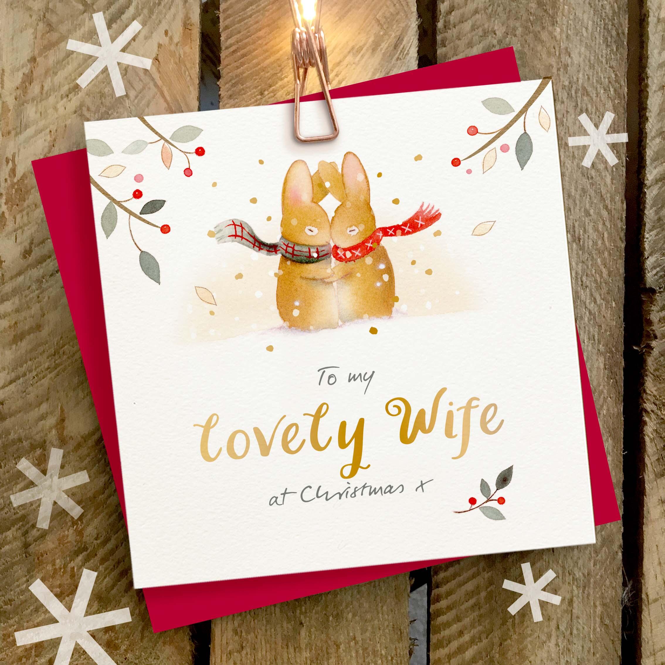 Christmas card featuring a large gold foil ‘Lovely Wife’ caption and a cuddling rabbit couple wearing woolly scarves.