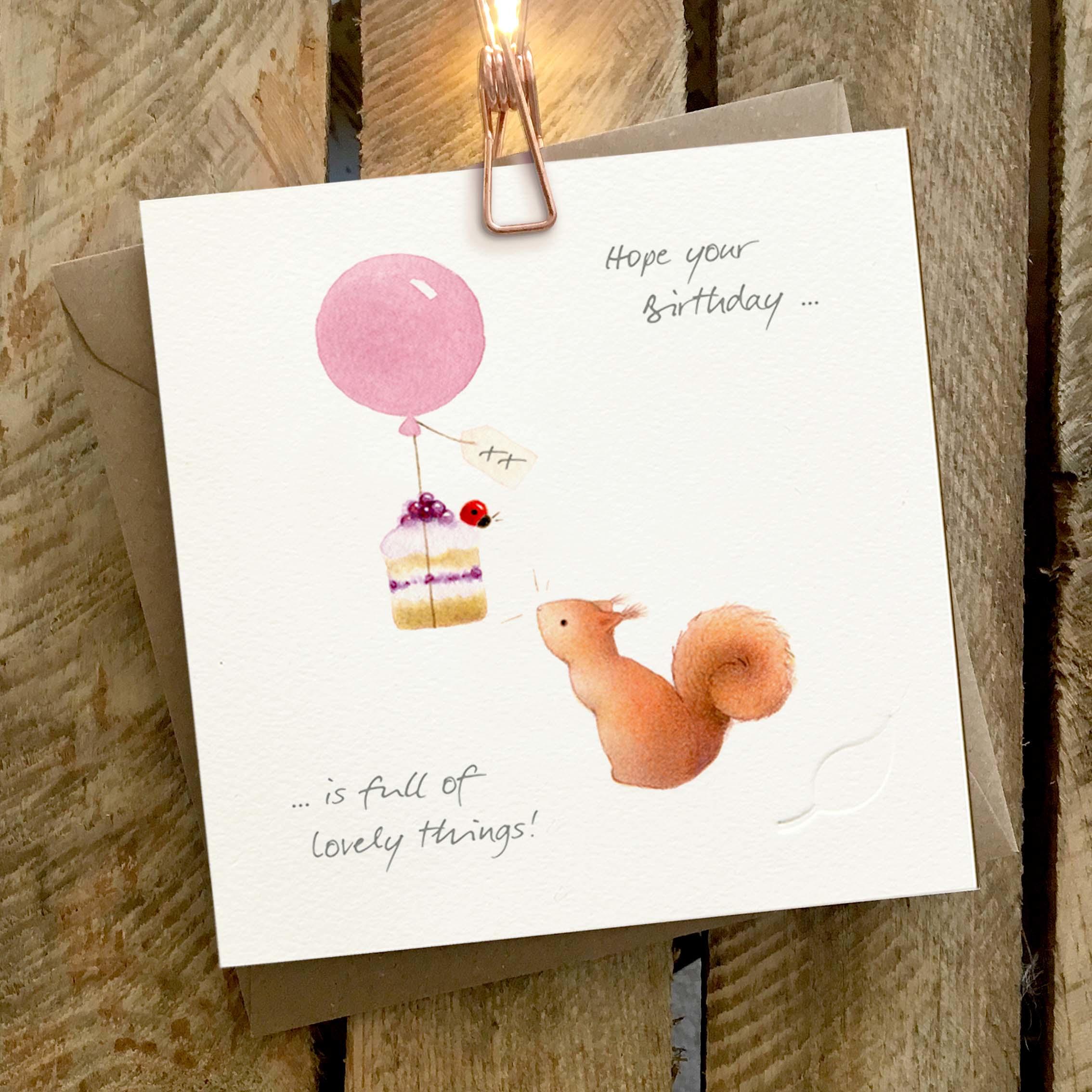 Card featuring a cute squirrel and a cake tied beneath a floating balloon with a ladybird sitting on the cake.