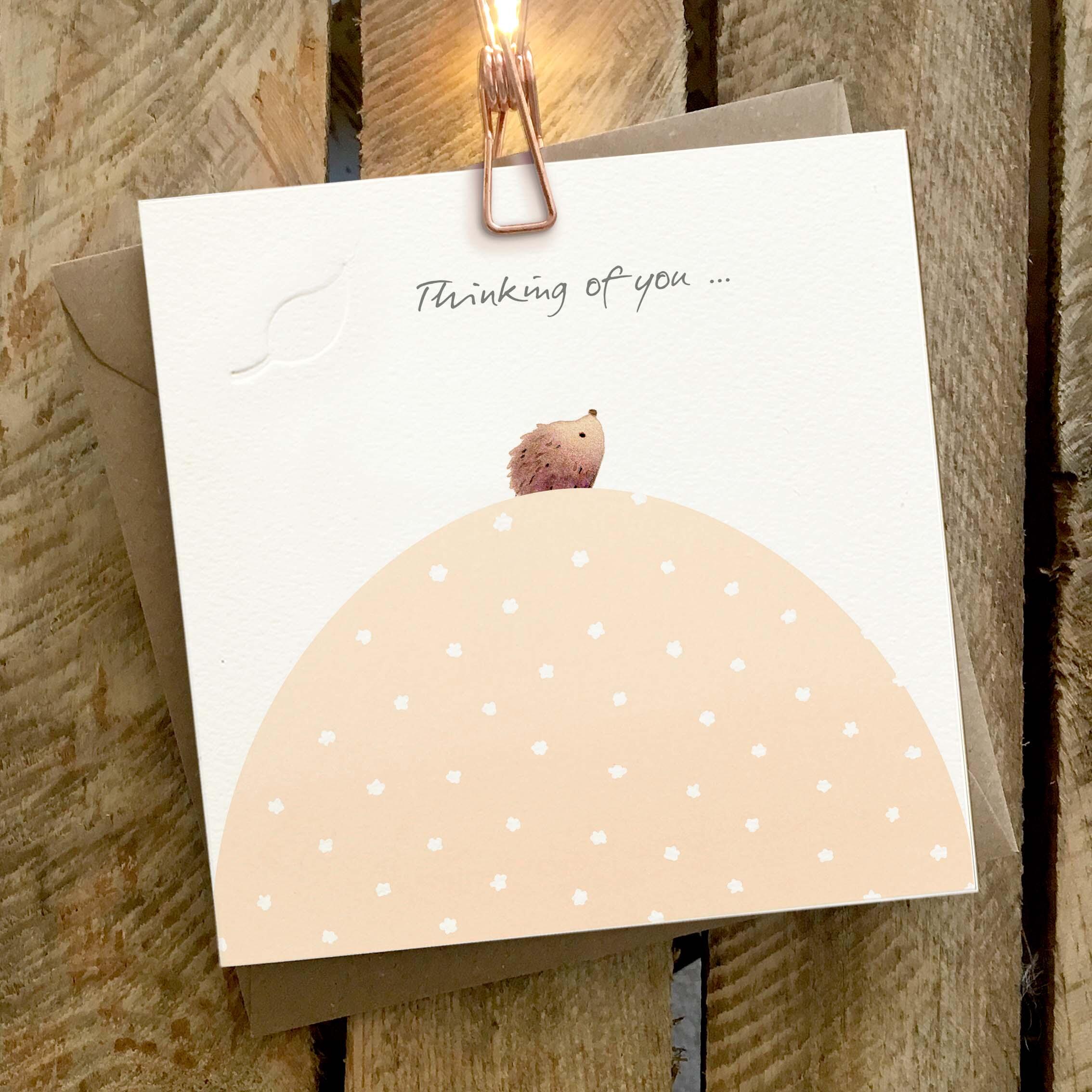 Card featuring a cute tiny little hedgehog sitting on top of a hill. Caption reads ‘Thinking of You’.