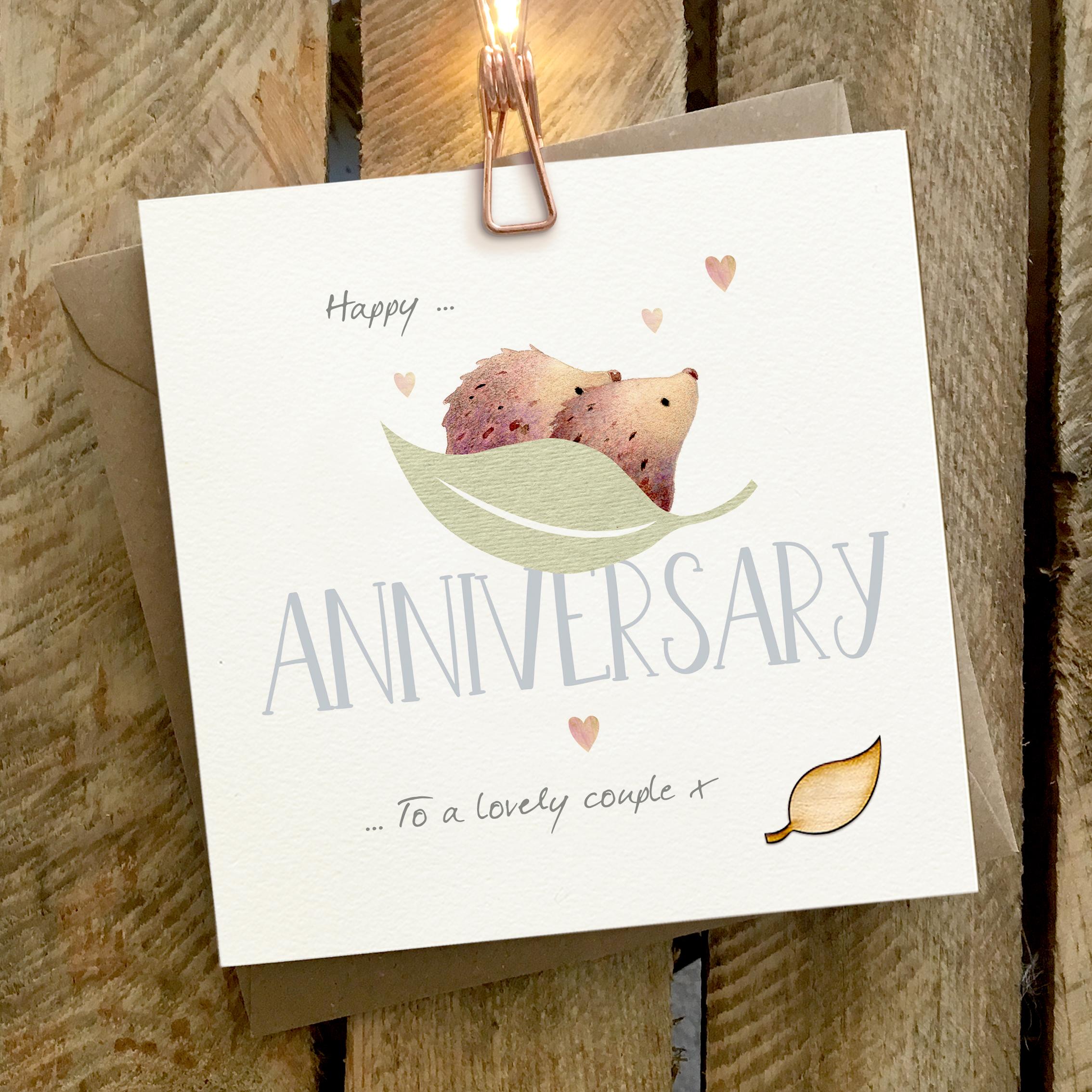 Card featuring two hedgehogs cuddling on a large leaf, sitting on top of a large ANNIVERSARY caption
