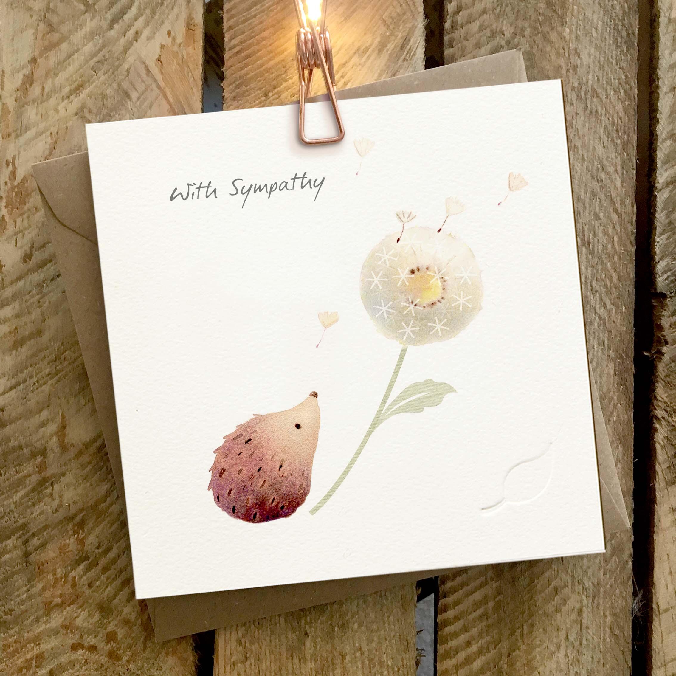 Card featuring a cute hedgehog and dandelion clock. Caption reads ‘With Sympathy’.