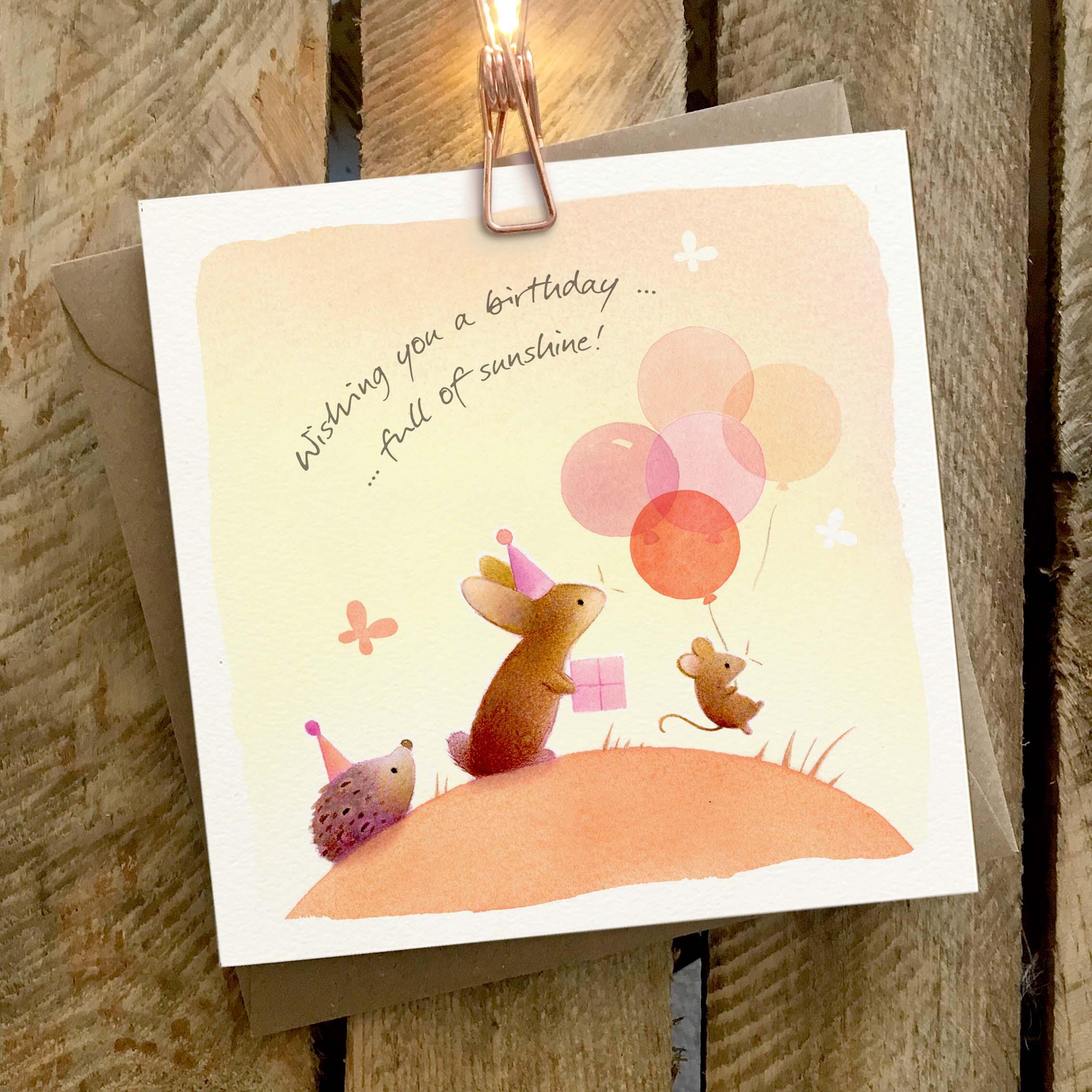 Greetings card featuring a group of animals with balloons on a sunny hill.