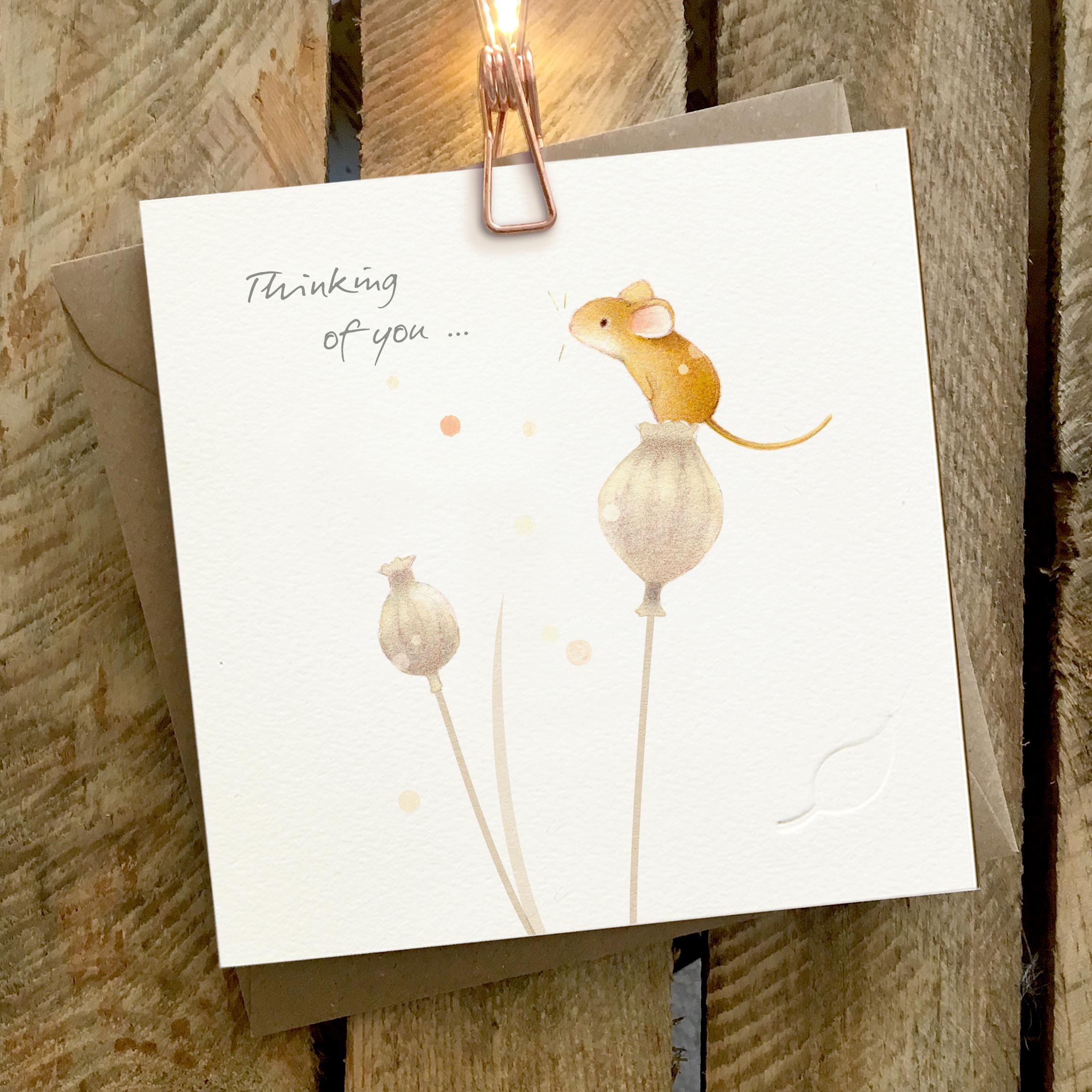 Card featuring a cute mouse sitting on top of a poppy seed head. Captions reads “Thinking of You”