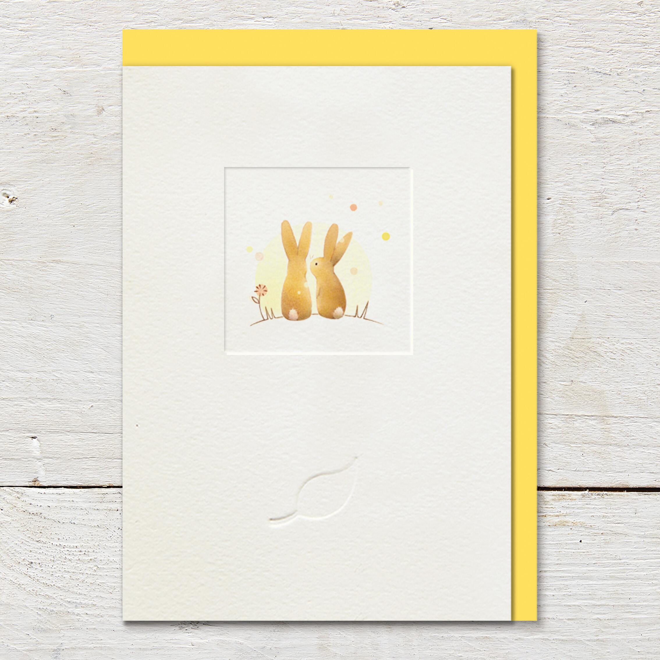Card featuring an illustration of two cute rabbits sitting on a sunny hillside in the middle of a small debossed window panel. Card is left blank for an open send