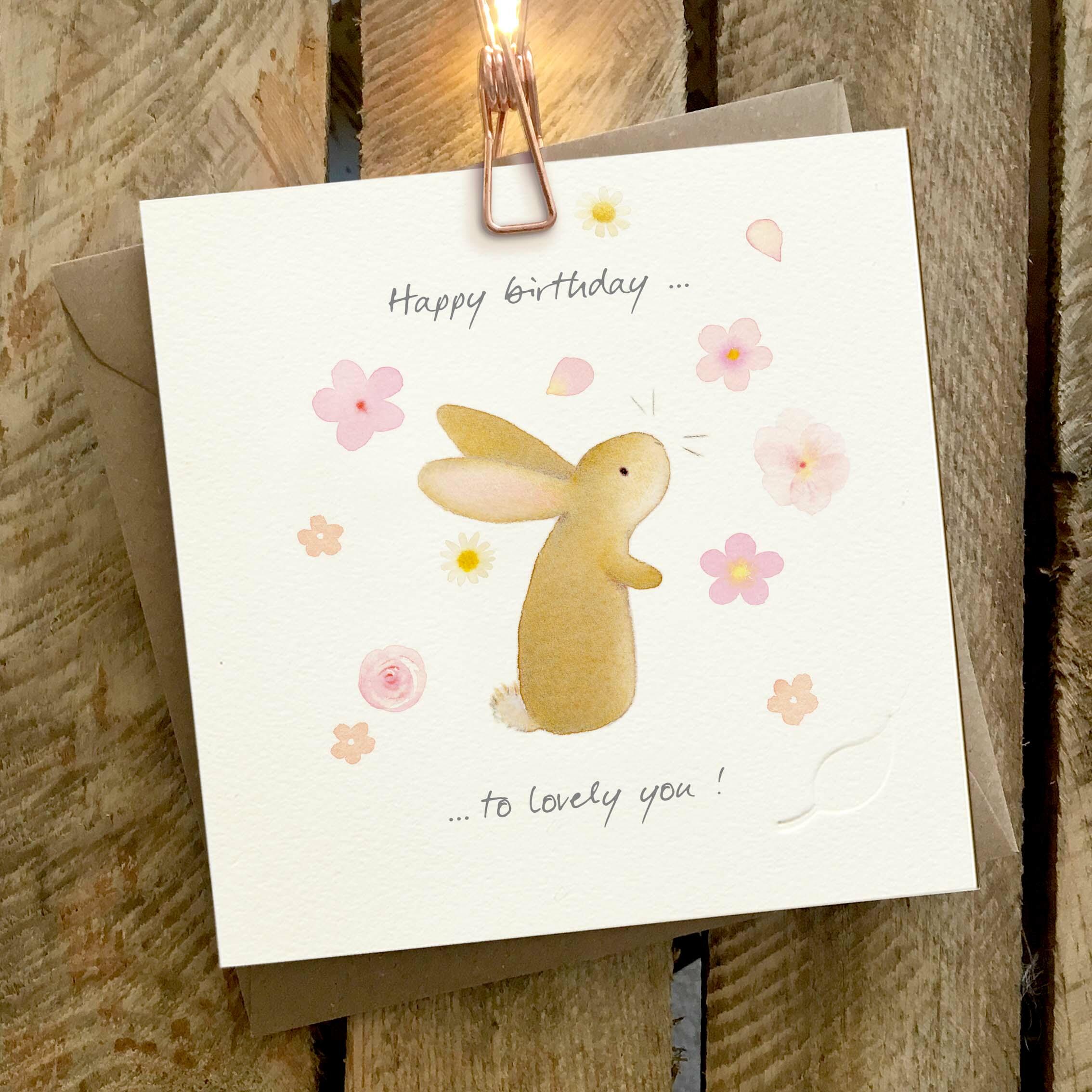 Card featuring a cute illustrated rabbit surrounded by falling flowers. Caption reads ‘Happy birthday to lovely you’..