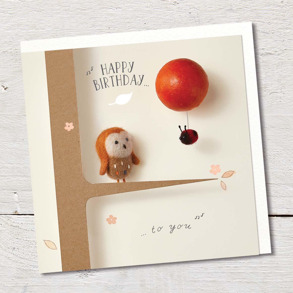 Card featuring a cute felted owl sitting in a tree, and looking at a tiny ladybird hanging onto a floating red balloon.