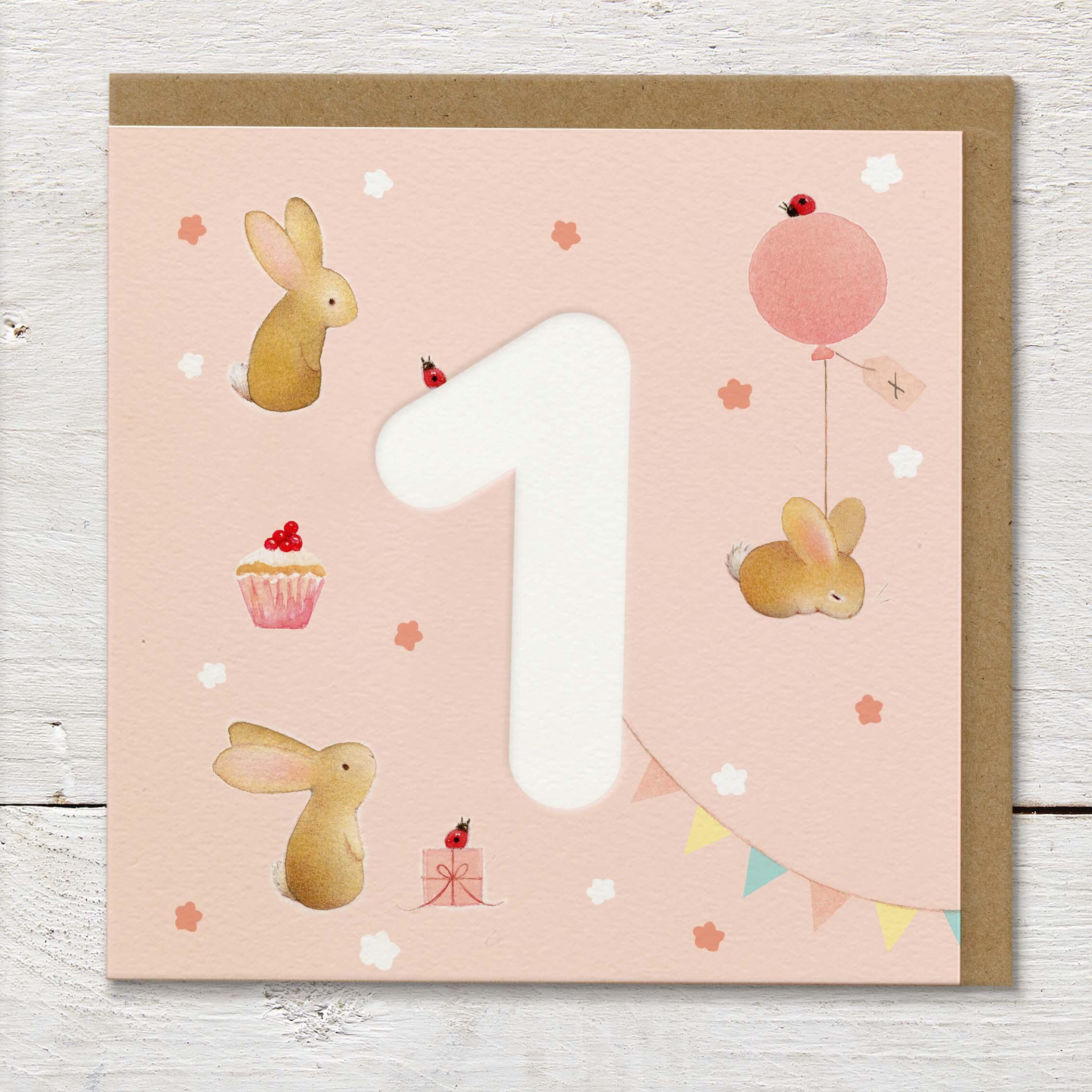 Children's age card featuring a large debossed age 1 surrounded by cute rabbits and party elements on a pale peach background.
