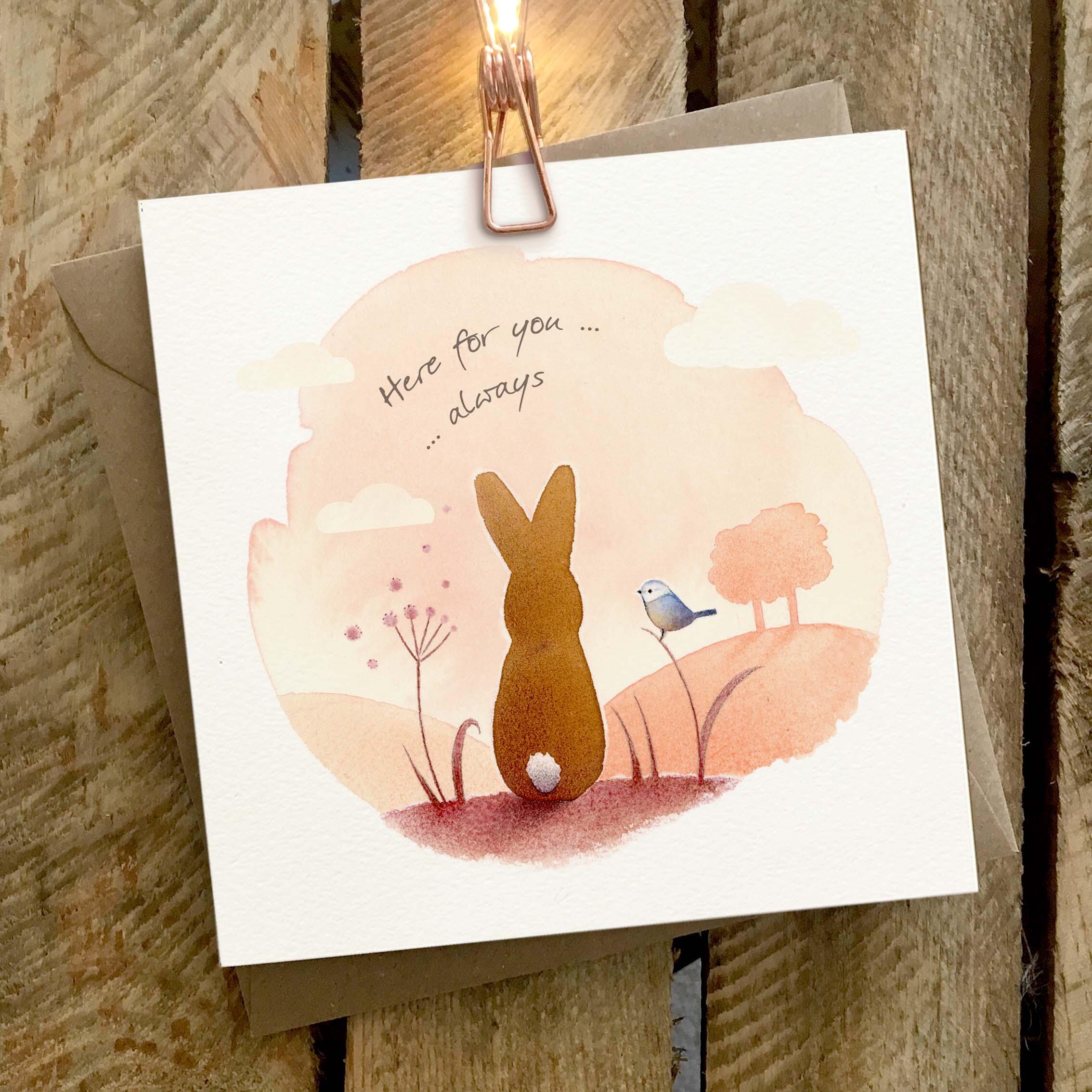 Greetings card featuring a rabbit and bird on a sunlit hillside.