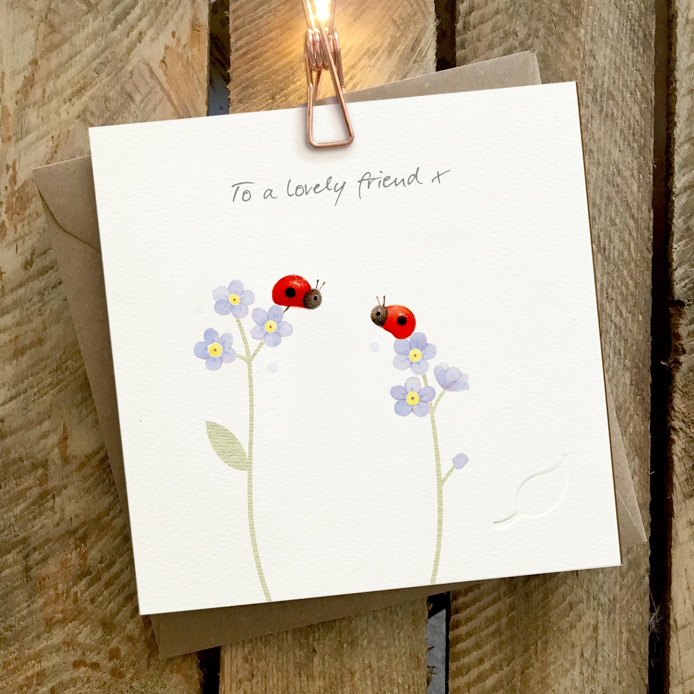 Card featuring two cute ladybirds sitting on top of forget-me-not flower heads. Caption reads “To a Lovely Friend X”