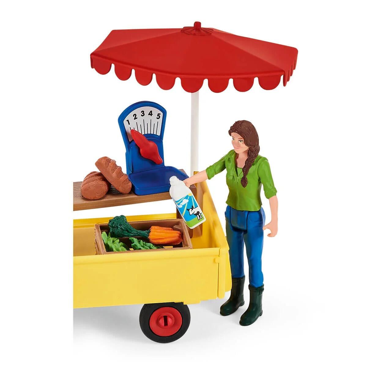 Close-up of the Schleich mobile farm stand with figure standing beside the yellow stall and red canopy.