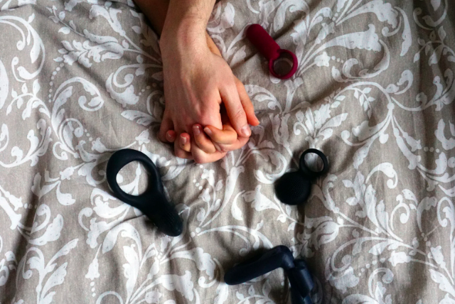 close up of sex toys on bed and couple holding hands