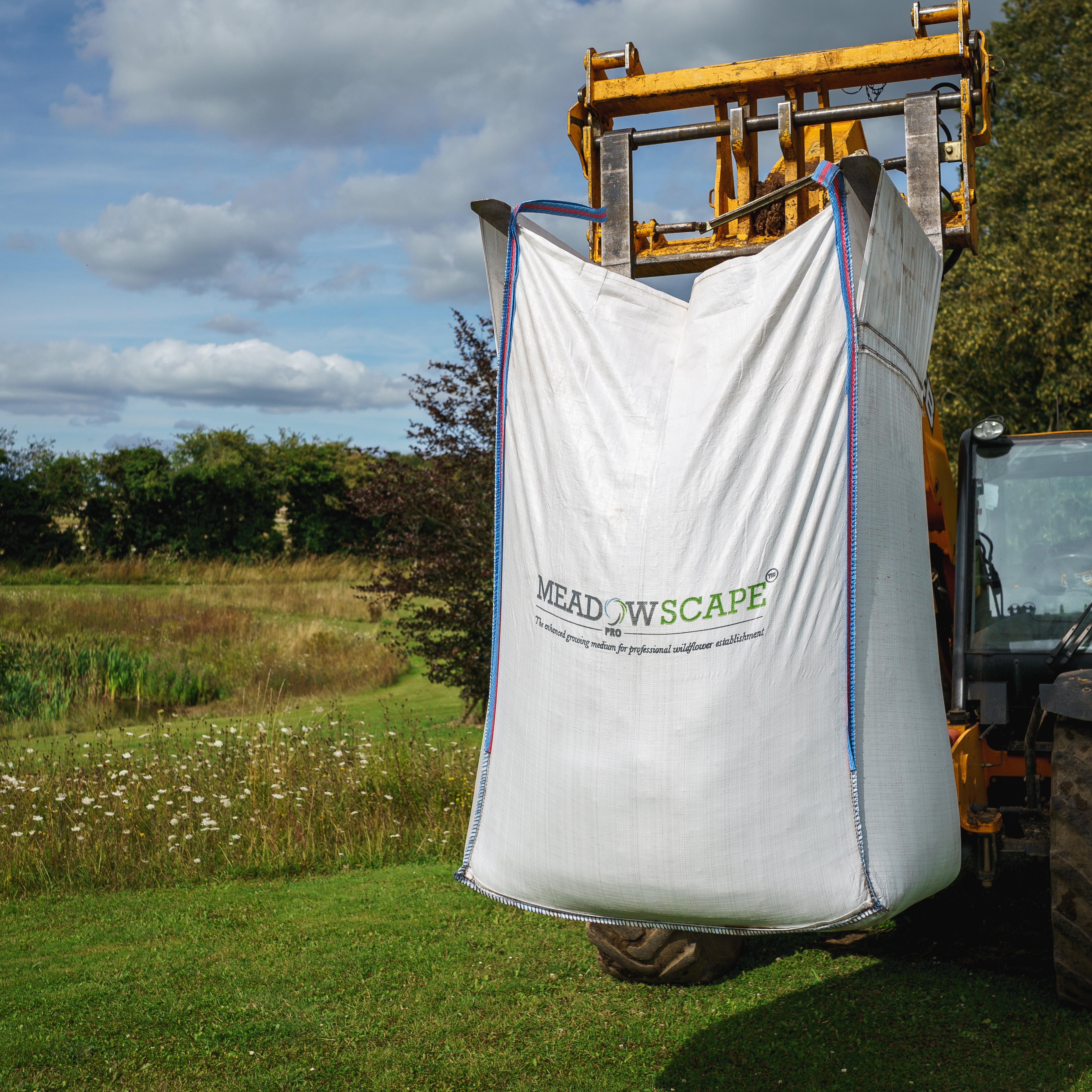 A large dumpy bag of Meadowscape Pro held up by a forklift with wildflowers in the background