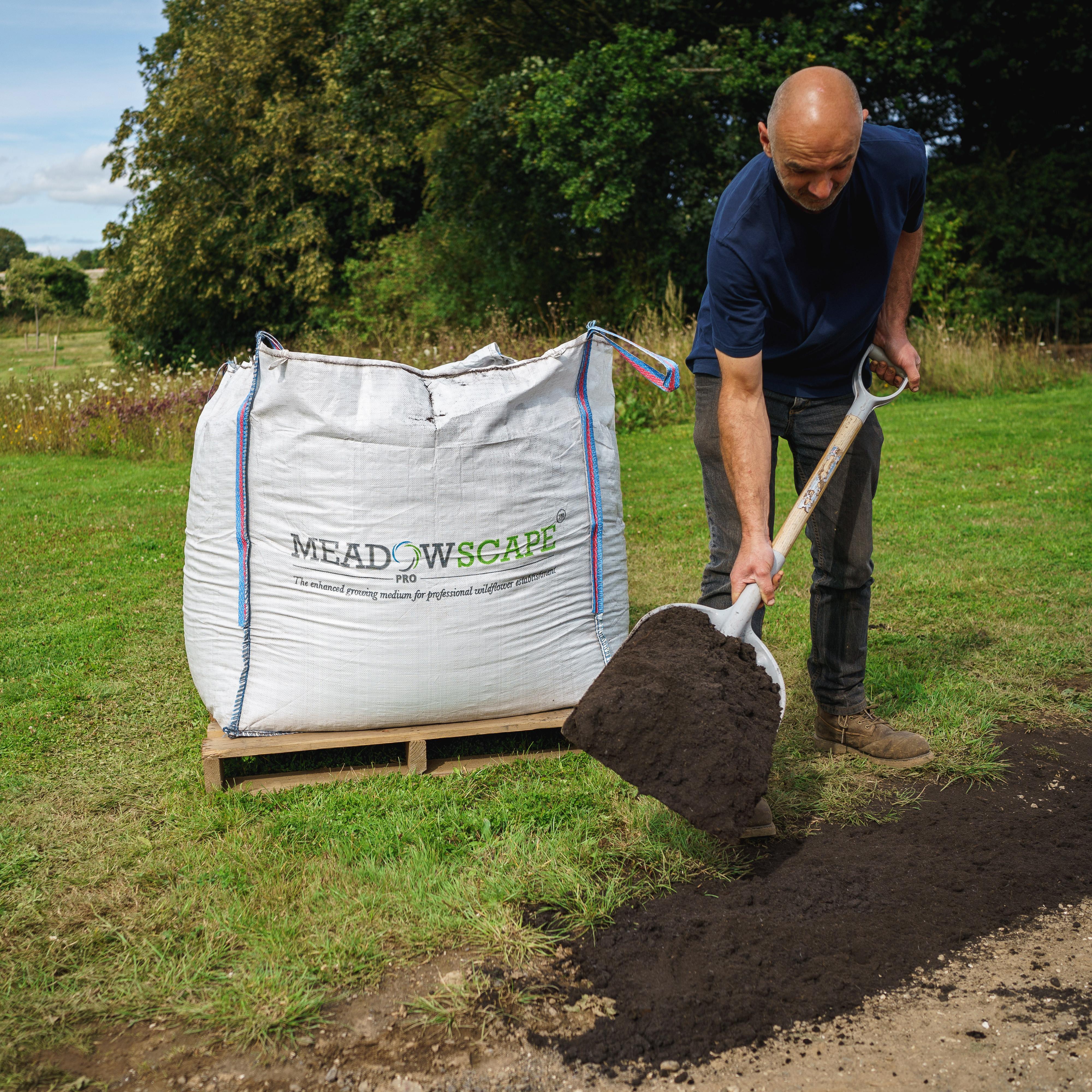 A man spreading Meadowscape Pro on the ground from a dumpy bag of product