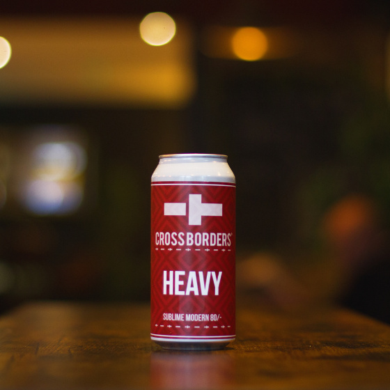 A can of beer with a burgandy label, Heavy, on a wooden table.