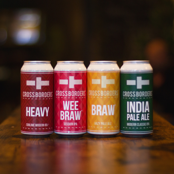 4 cans of beer with different coloured labels, one burgandy, one yellow, one pink, and one green, sitting shoulder to shoulder on a dark wooden table.