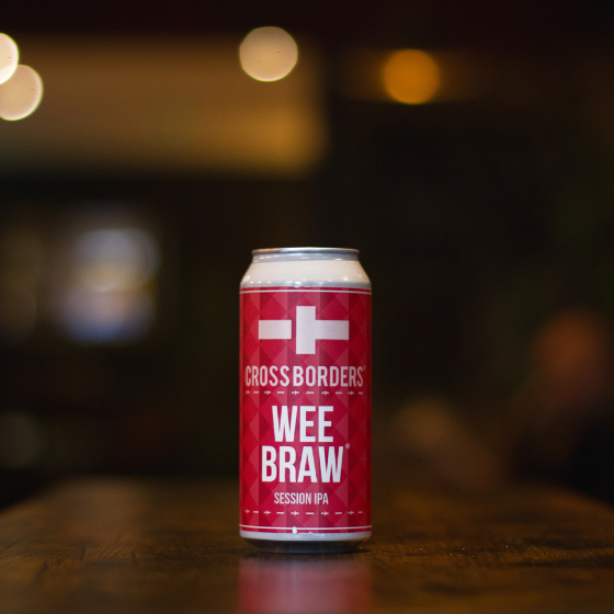 Can of beer with a pink label which reads "Wee Braw" sitting on a wooden table.