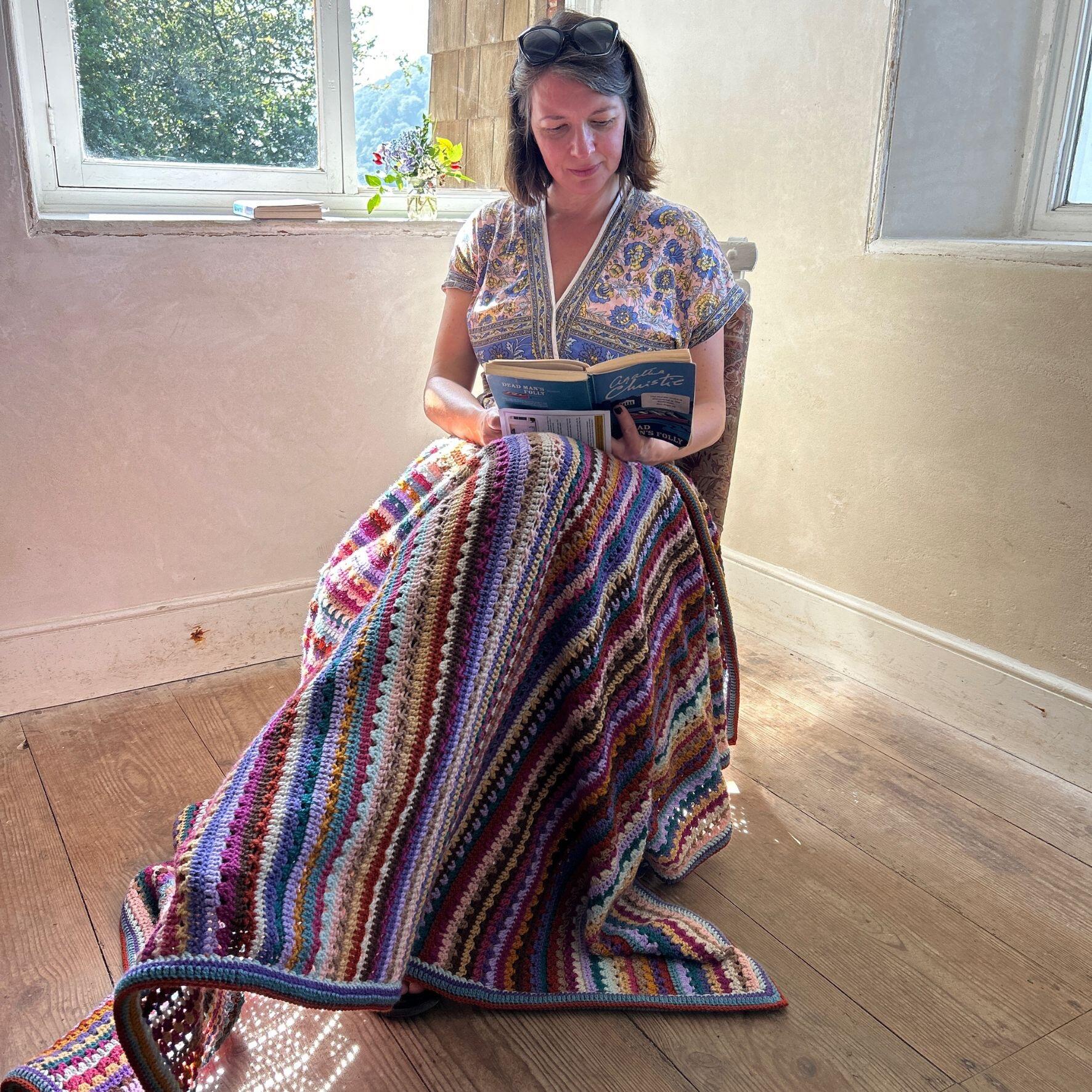 Anja sitting on Agatha Christie's chair with the greenway blanket and reading a book