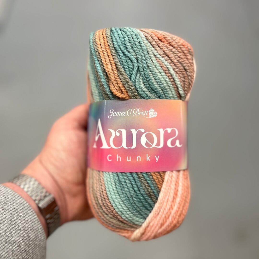 James C Brett Aurora Chunky self-striping yarn ball showing soft blended shades of teal, peach, and brown, ideal for chunky crochet and knitting projects.