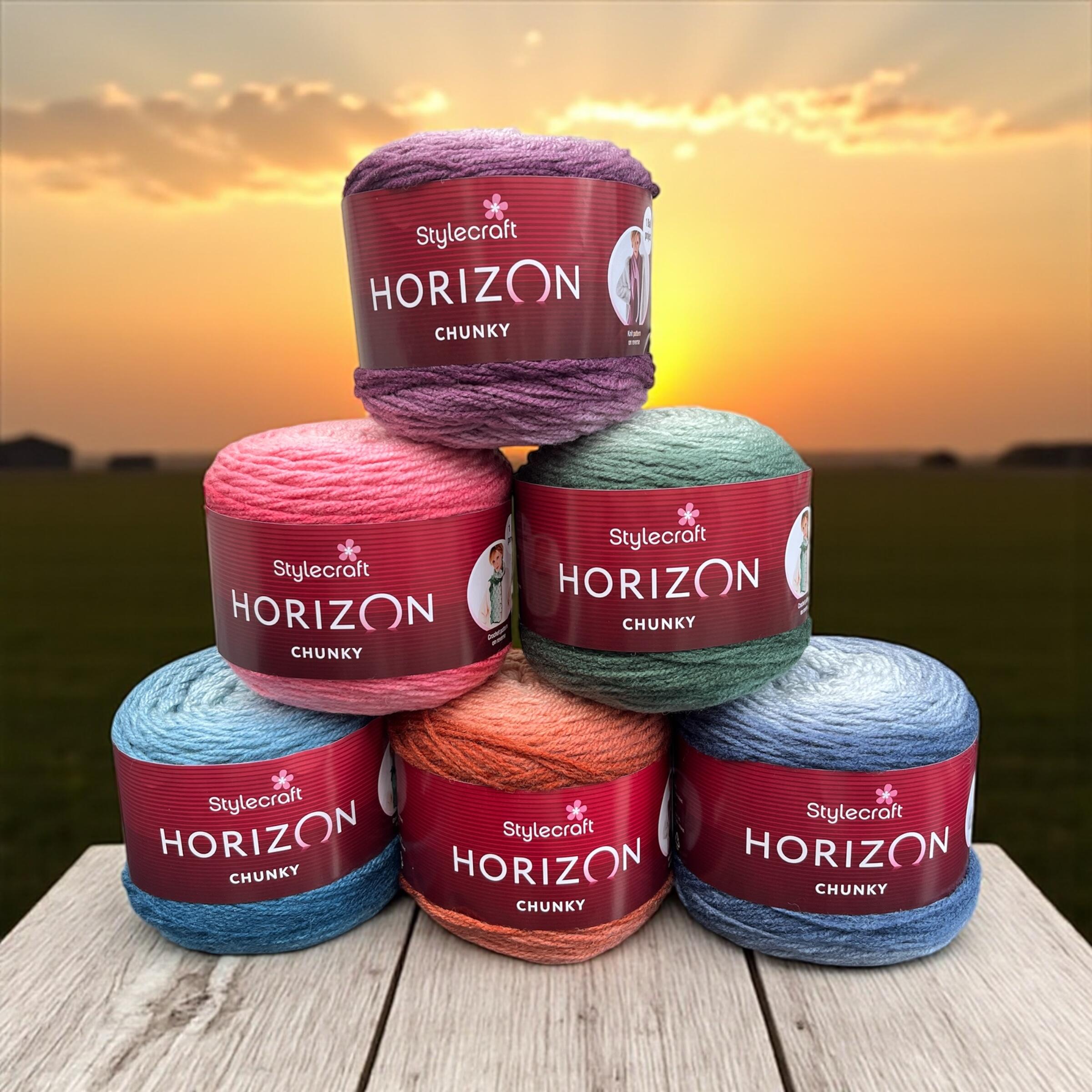 Stylecraft Horizon Chunky yarn collection – Six 200g gradient cakes in shades Indigos, Pinks, Plums, Greens, Russets, and Teals displayed on a wooden table with a sunset Horizon.