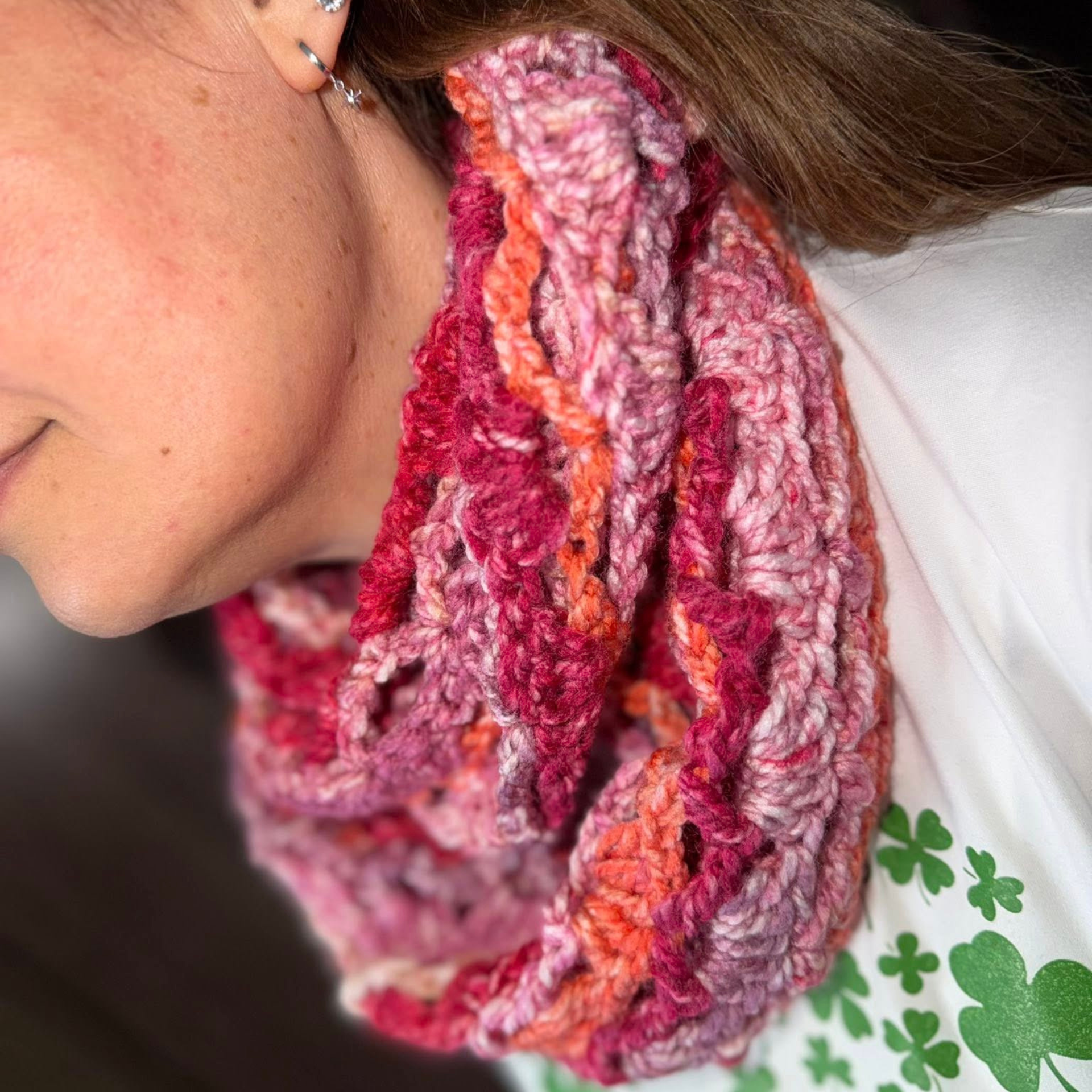 Close-up of the Rachel crochet cowl made with King Cole Hedgerow Chunky yarn in the Holly Berry shade, showing rich variegated tones of pink, berry red, and warm coral with a thick, textured stitch pattern worn snugly around the neck.