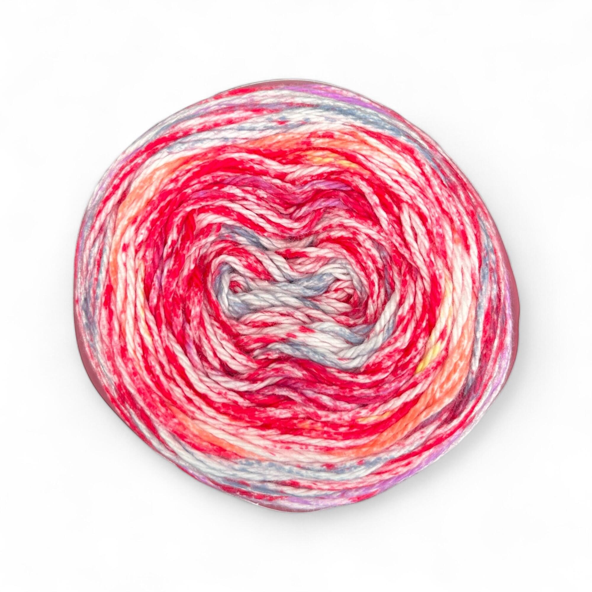 James C. Brett Cotton Waves yarn cake in Sunset Sorbet WV01 – 100% cotton DK yarn with pink, coral, purple, yellow, and white tones.