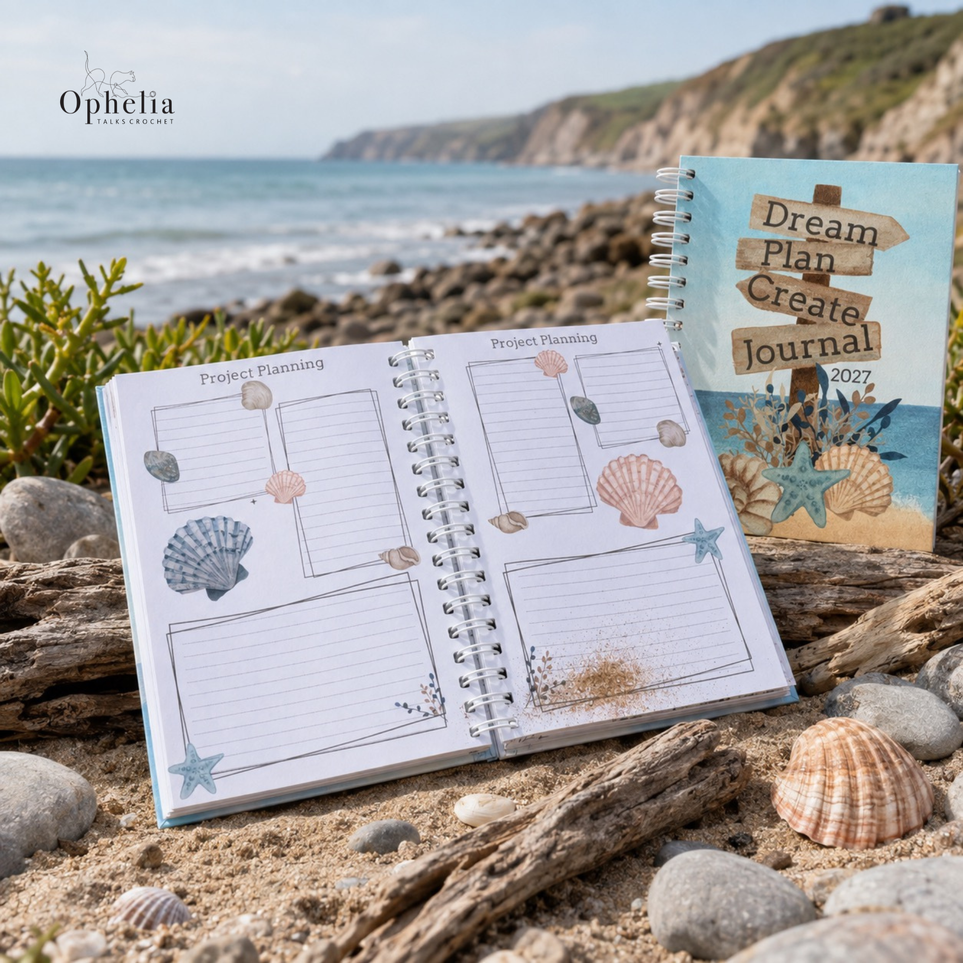 Dream Plan Create Journal open to the illustrated project planning pages on a rocky Devon beach, with driftwood, seashells, sea and coastal cliffs behind.