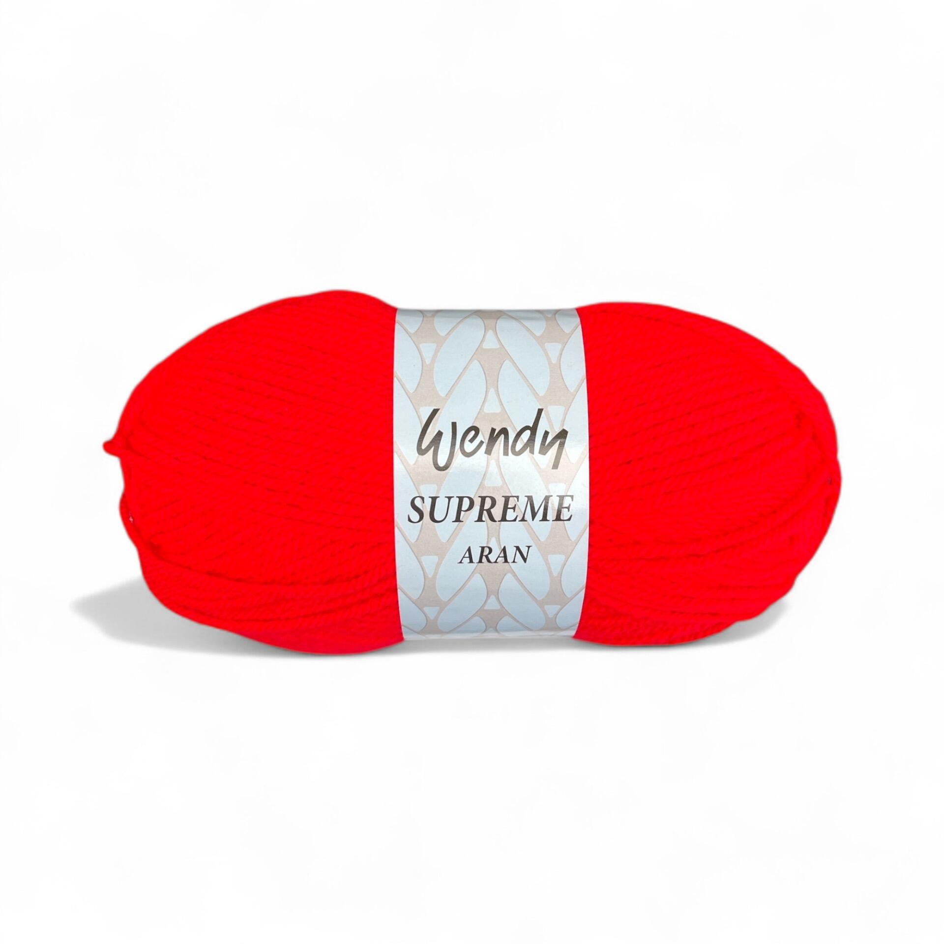 A skein of Wendy Supreme Aran yarn in Red (SA15), a vivid and bold red shade, wrapped in its branded label, displayed against a white background. The label features the "Wendy Supreme Aran" name with a decorative pattern.