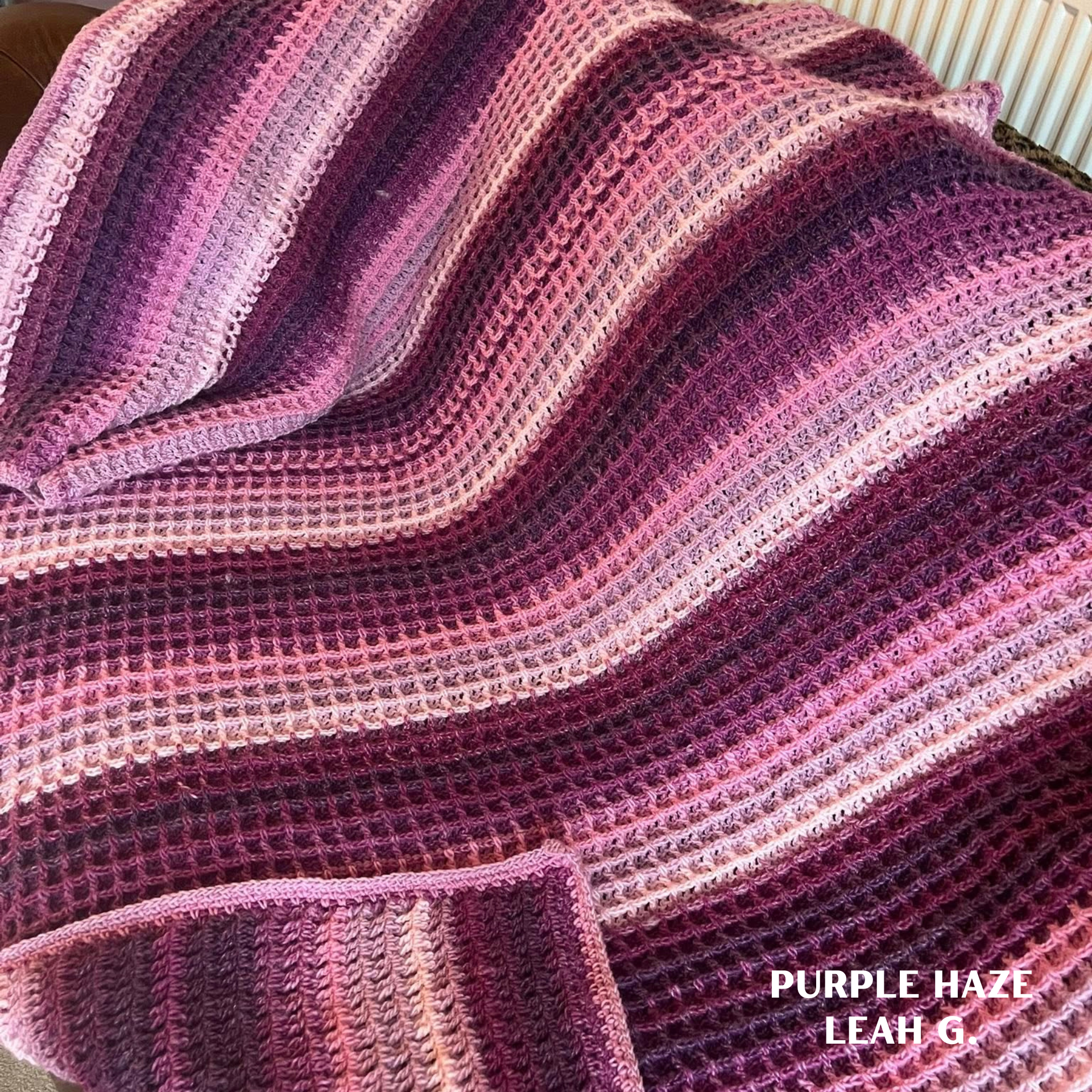 Crocheted waffle stitch blanket made in Curiosity yarn shade Purple Haze, featuring rich purple, plum, and soft pink gradient stripes with a textured, cozy finish, draped over a sofa.