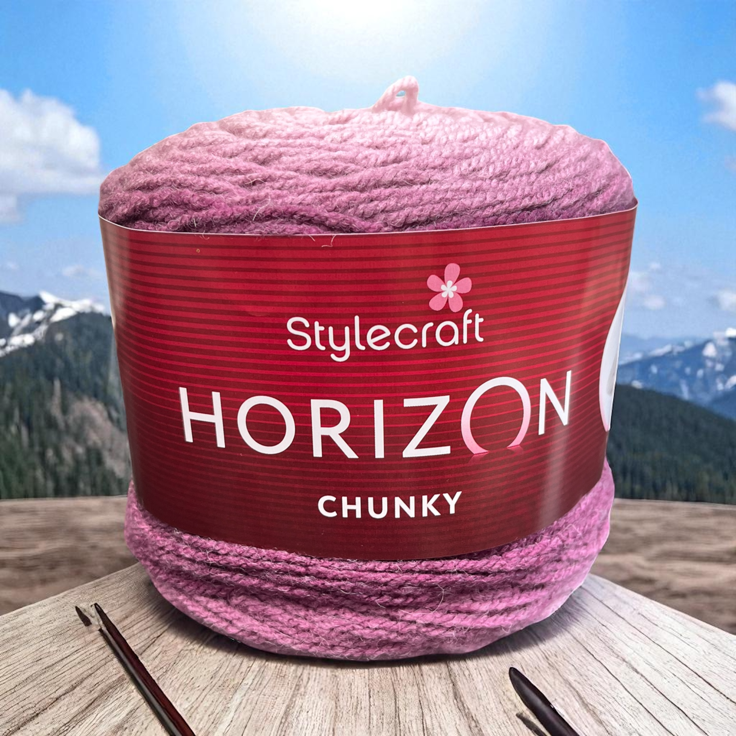 Stylecraft Horizon Chunky yarn ball in shade Plums displayed on a wooden table with crochet hooks and a mountain horizon in the background