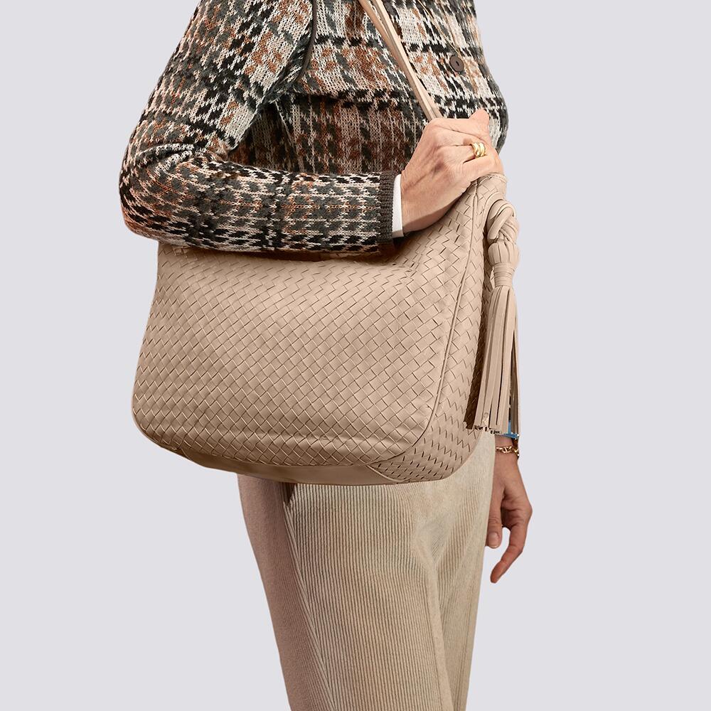 Stylish lady in plaid jacket and pants holding an elegant beige woven leather handbag, with double shoulder straps and long tassel on the side.