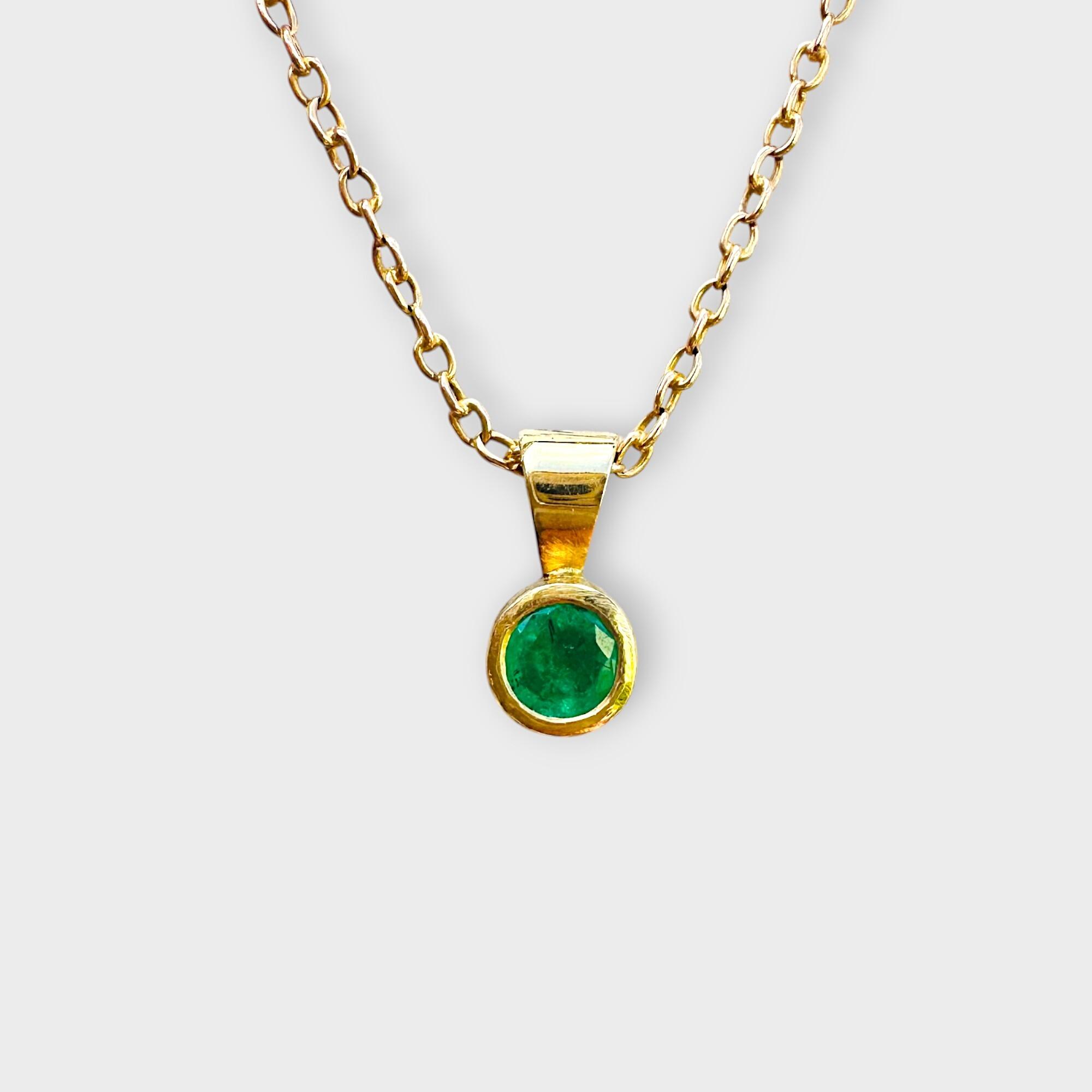Front view of 18ct gold emerald solitaire pendant with a round bezel-set emerald.