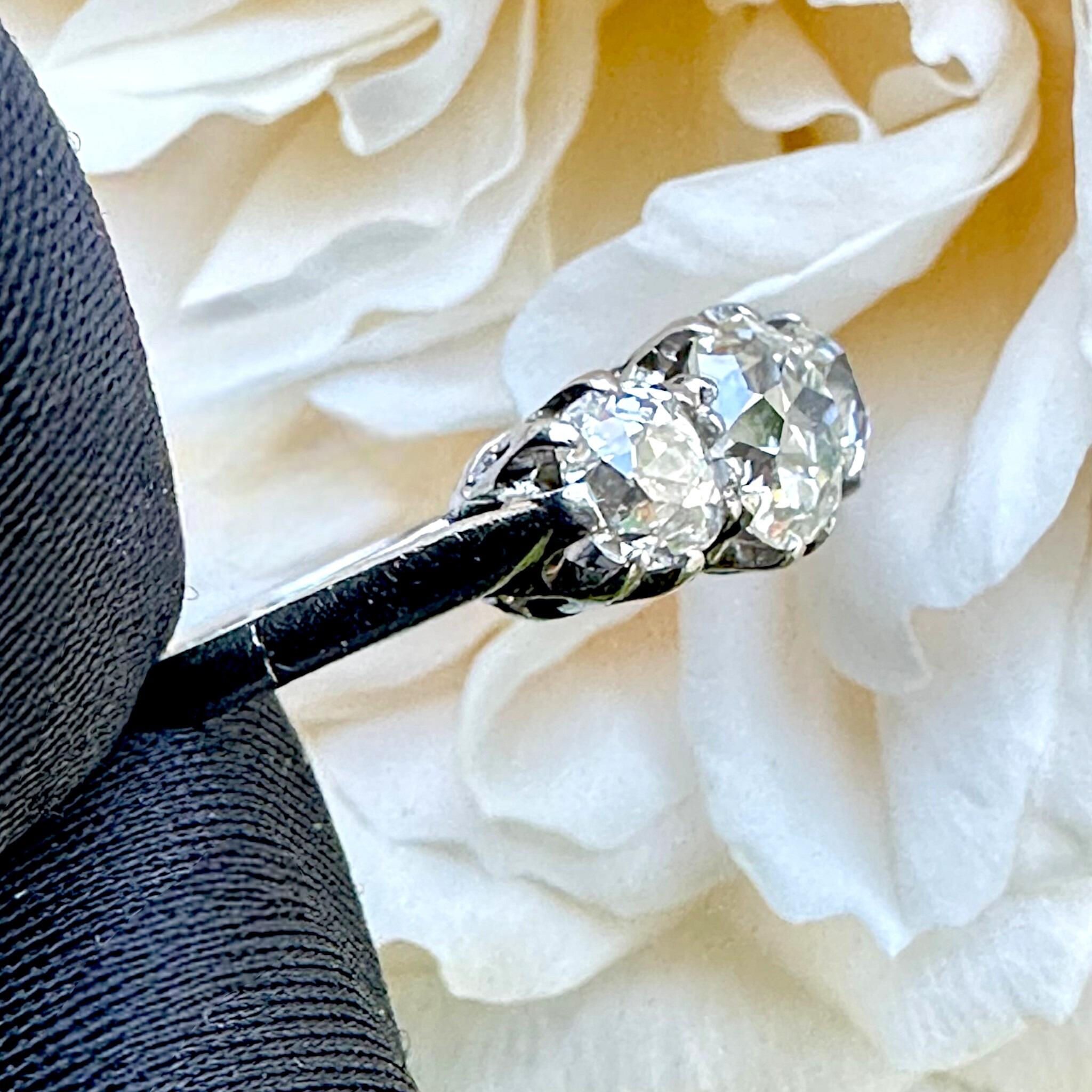 side view of Antique Platinum Old Cushion Cut Diamond Trilogy Ring with flower in the background