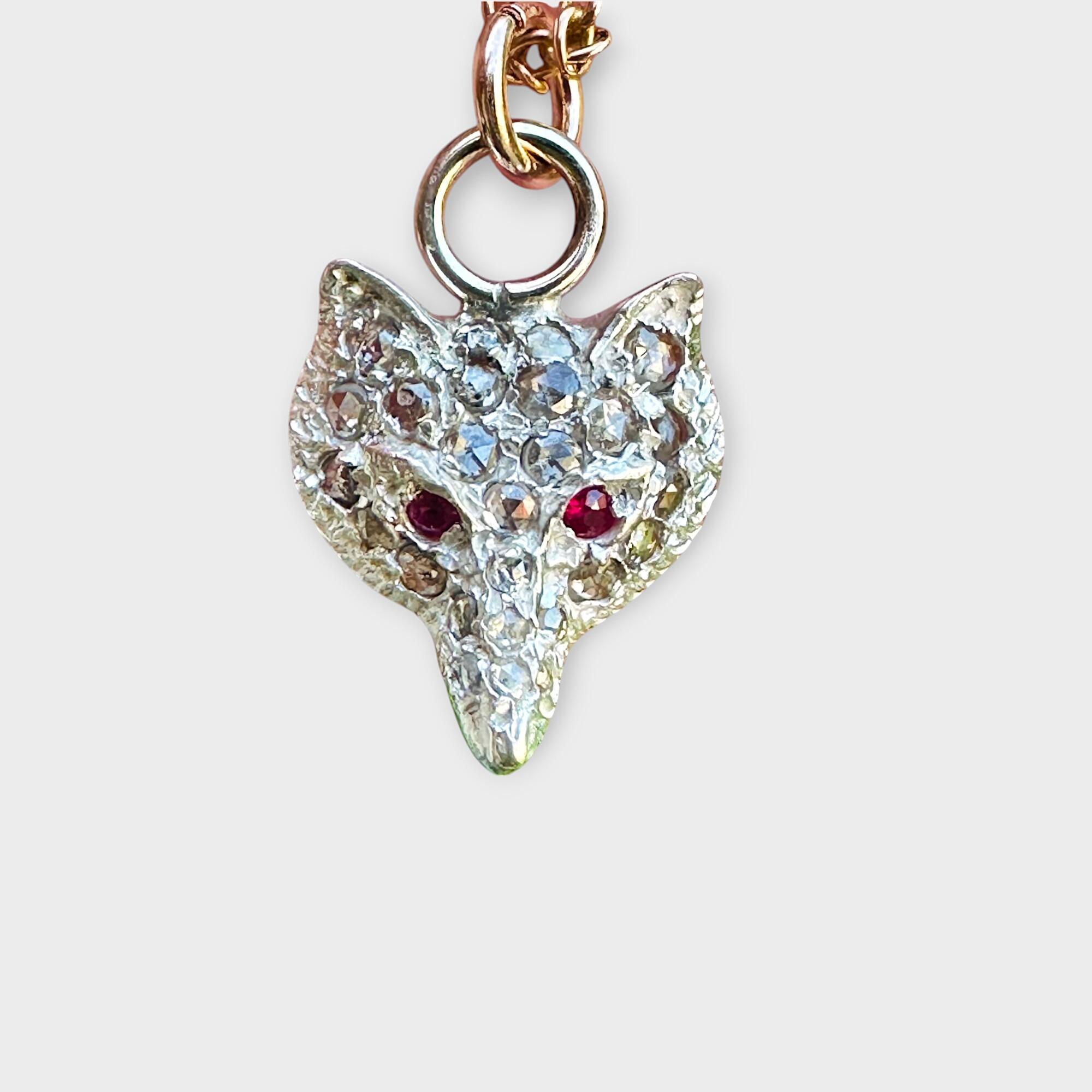 Vintage fox head pendant adorned with rose-cut diamonds in silver, accented by ruby eyes and 9ct rose gold fittings, close up on grey background.