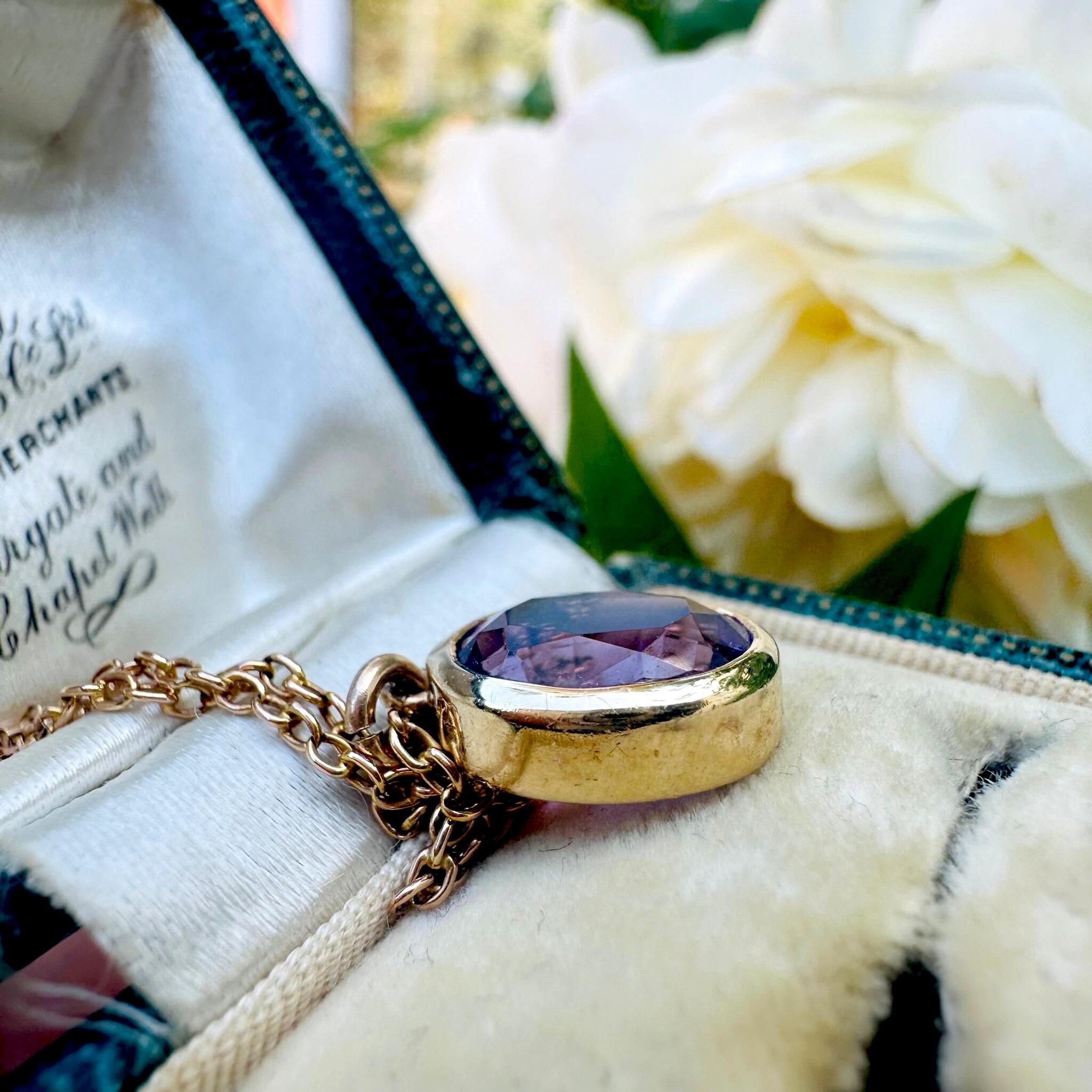 side profile of 14k Yellow Gold & Amethyst Pendant, laying on antique box with flowers in background