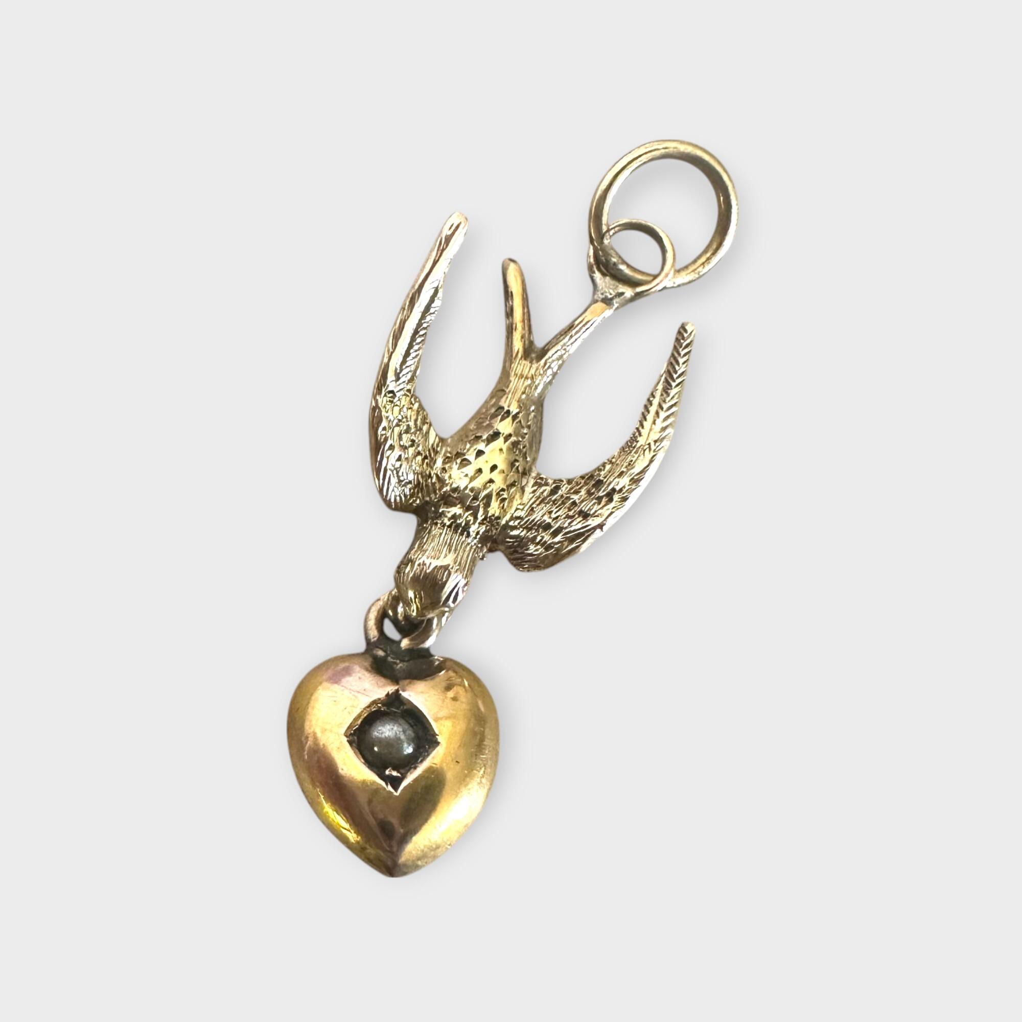 Art Nouveau gold swallow necklace holding a pearl heart – a symbol of love and safe return, grey background.
