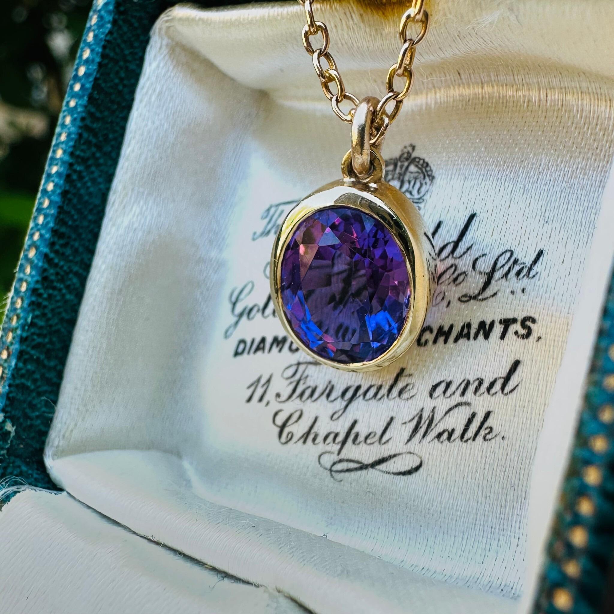 14k Yellow Gold & Amethyst Pendant hanging from gold chain on antique box