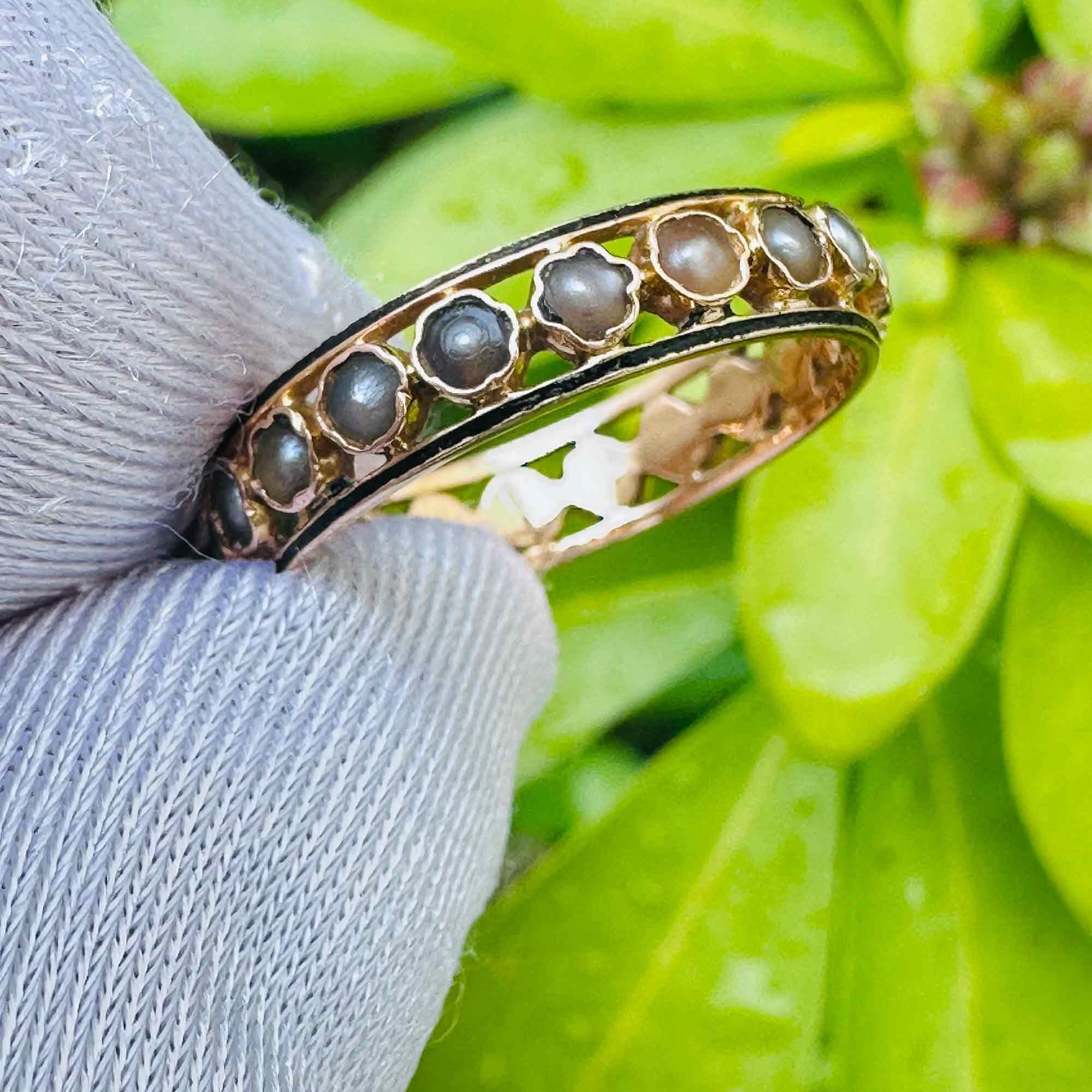 Antique, French 18ct, 18k, 750 Gold Natural Pearl & Enamel ring  side view held in white gloved hand with leaves in background.