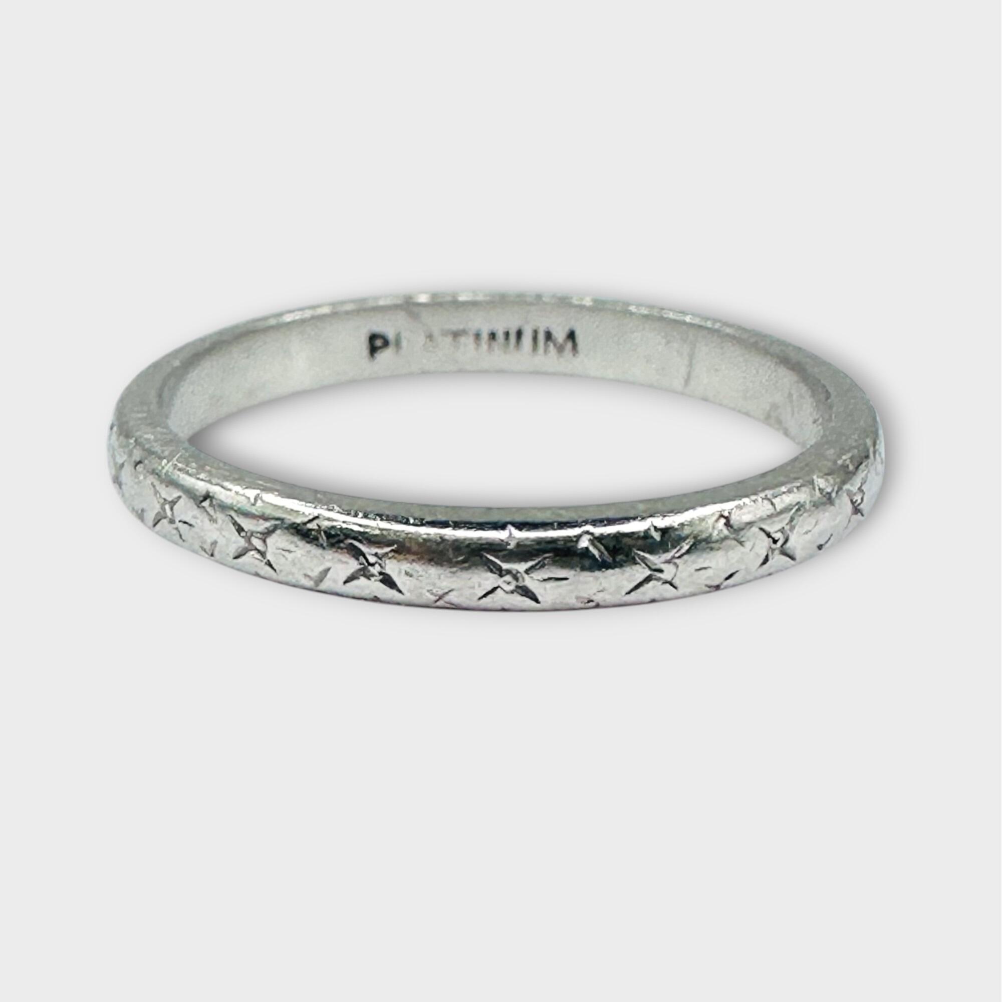 Antique platinum wedding band with engraved pattern on grey background.