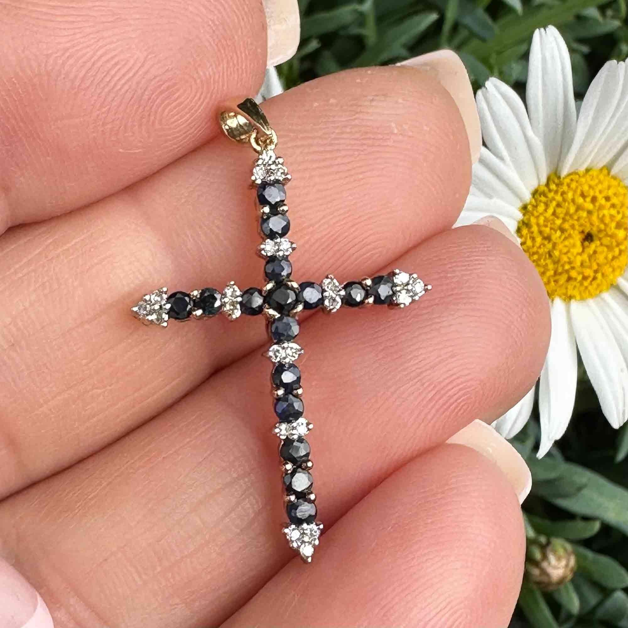 Sapphire and diamond cross in 9ct yellow gold on hand with garden background.