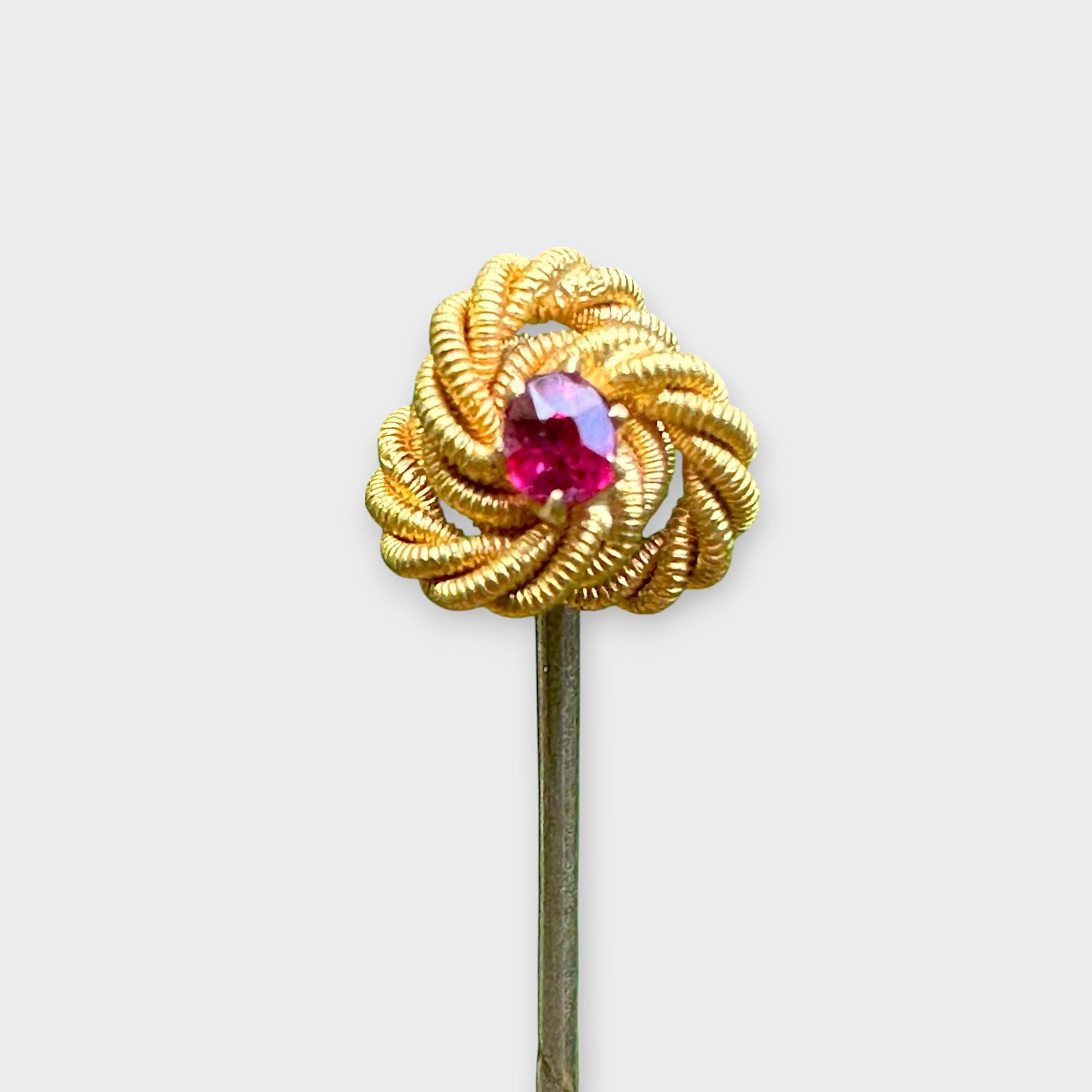 Edwardian 15ct gold lover’s knot stick pin with ruby in claw setting with grey background.