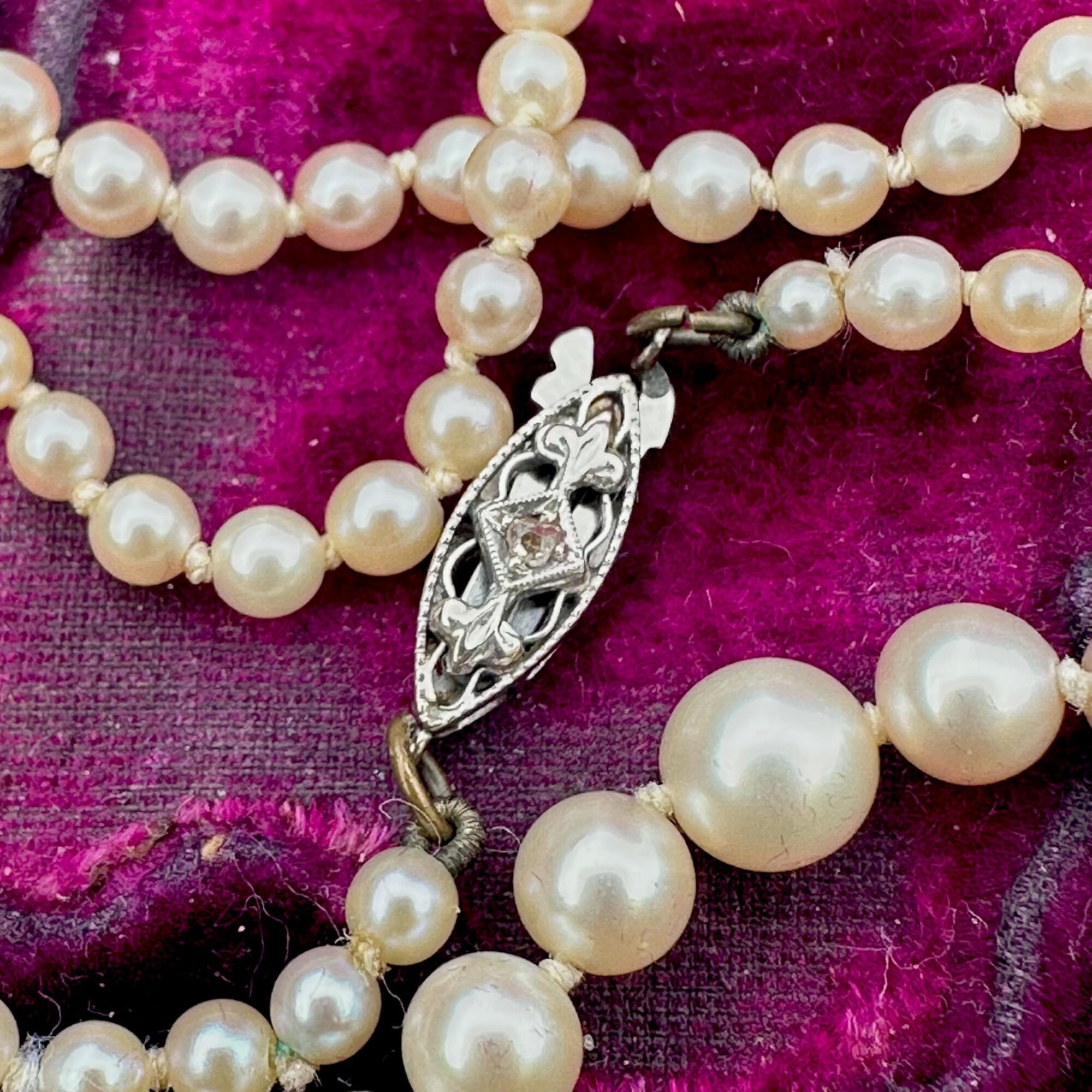 Art Deco cultured saltwater pearl necklace with graduated pearls and diamond-set 9k white gold clasp on purple velvet box with grey background.
